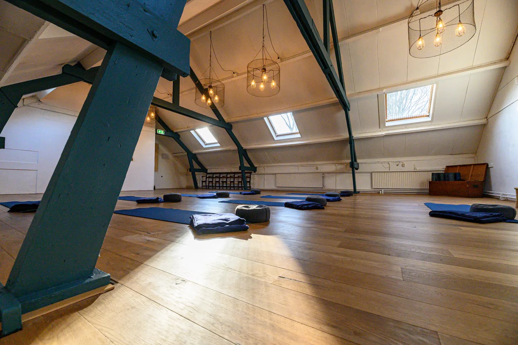 Yoga mats laid out on the wooden floor of a studio under the roof beams.