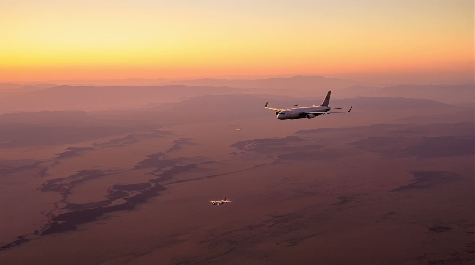 Illustration of grey fighter jets and a refueling tanker flying high over a hazy desert plateau at dusk.