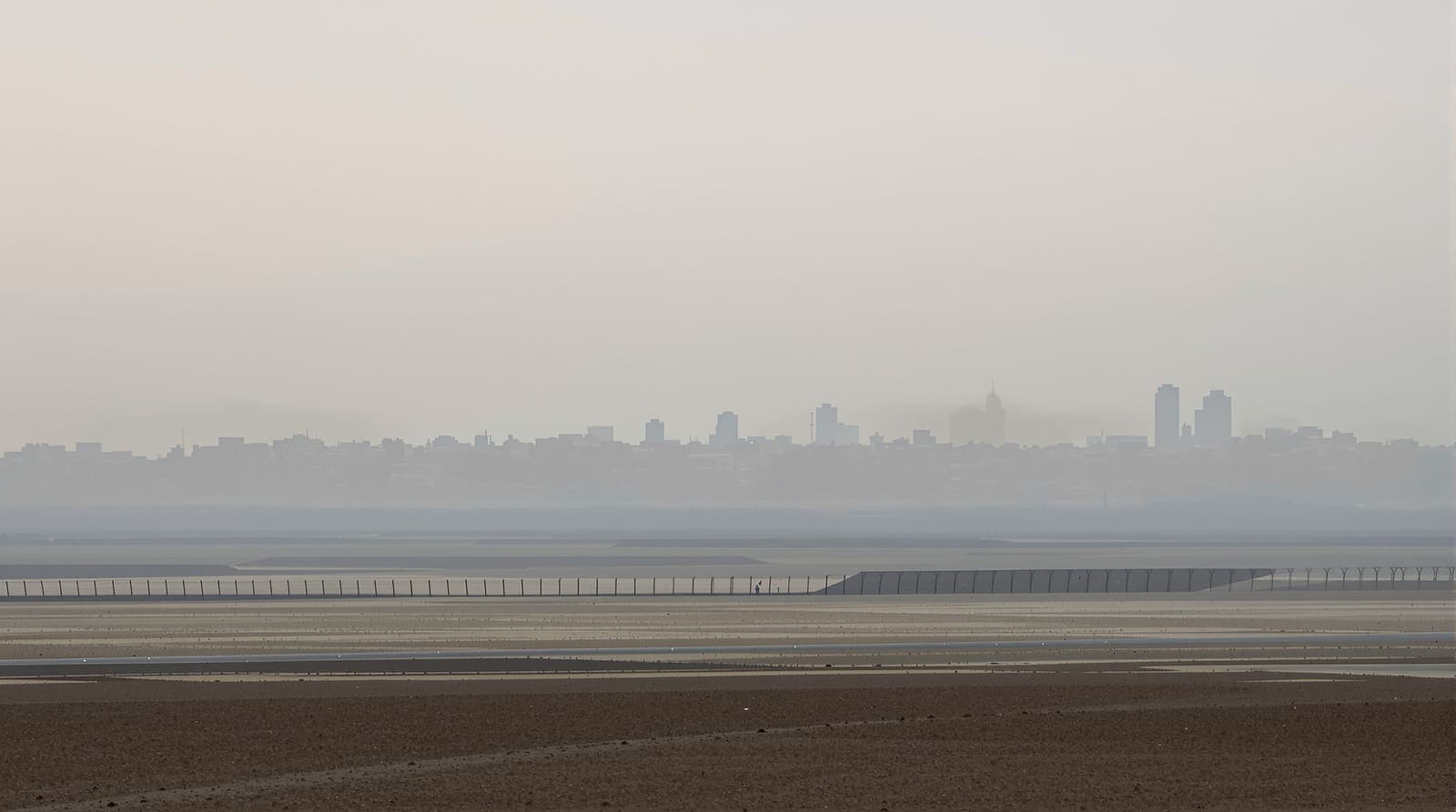 Illustration of the hazy Gaza skyline seen at dawn across flat farmland and a long border fence