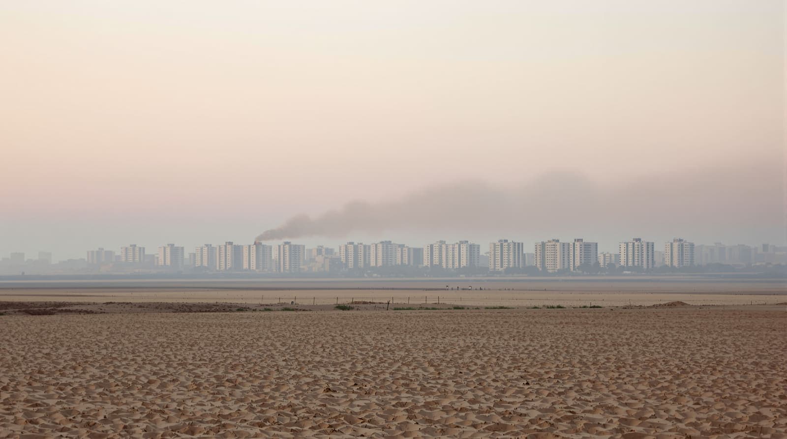 Illustration of the Gaza City skyline seen from a distance across sandy fields under a hazy overcast dawn sky.