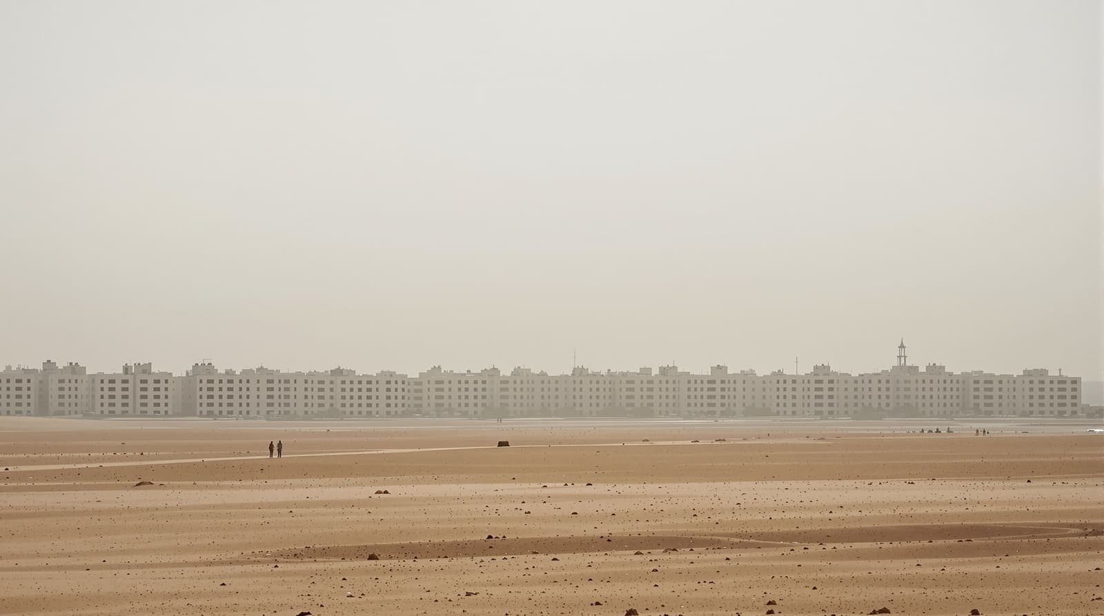 Illustration of the Gaza City skyline in grey dawn haze, seen from a distance across flat sandy ground.