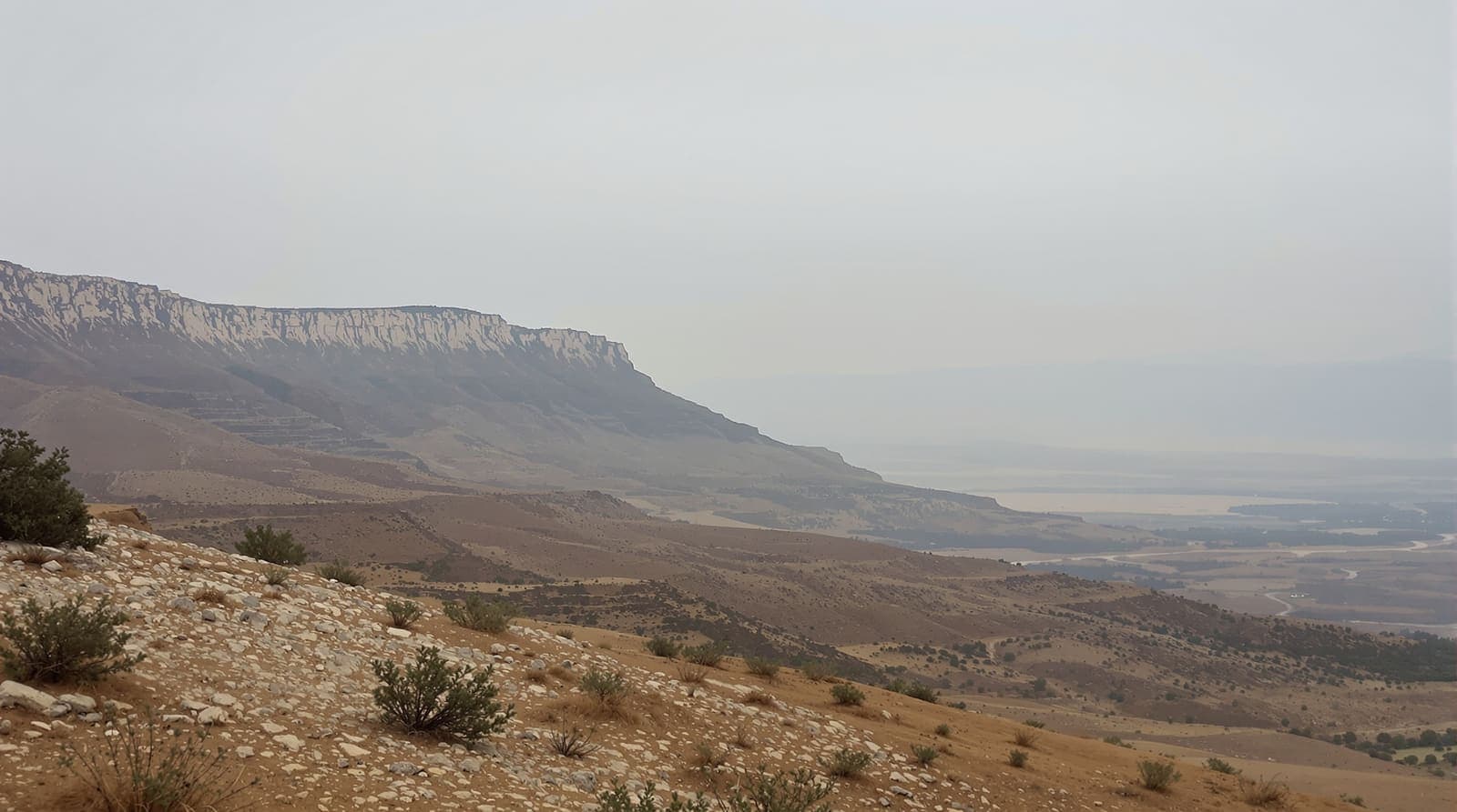Illustration of a limestone ridge in southern Lebanon seen across a wide valley at dawn, with dry scrub slopes and layered hills.