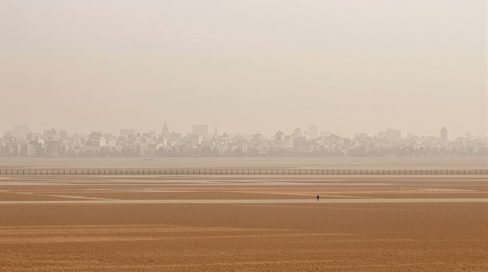 Illustration of the hazy northern Gaza skyline seen across flat farmland and a border fence at dawn