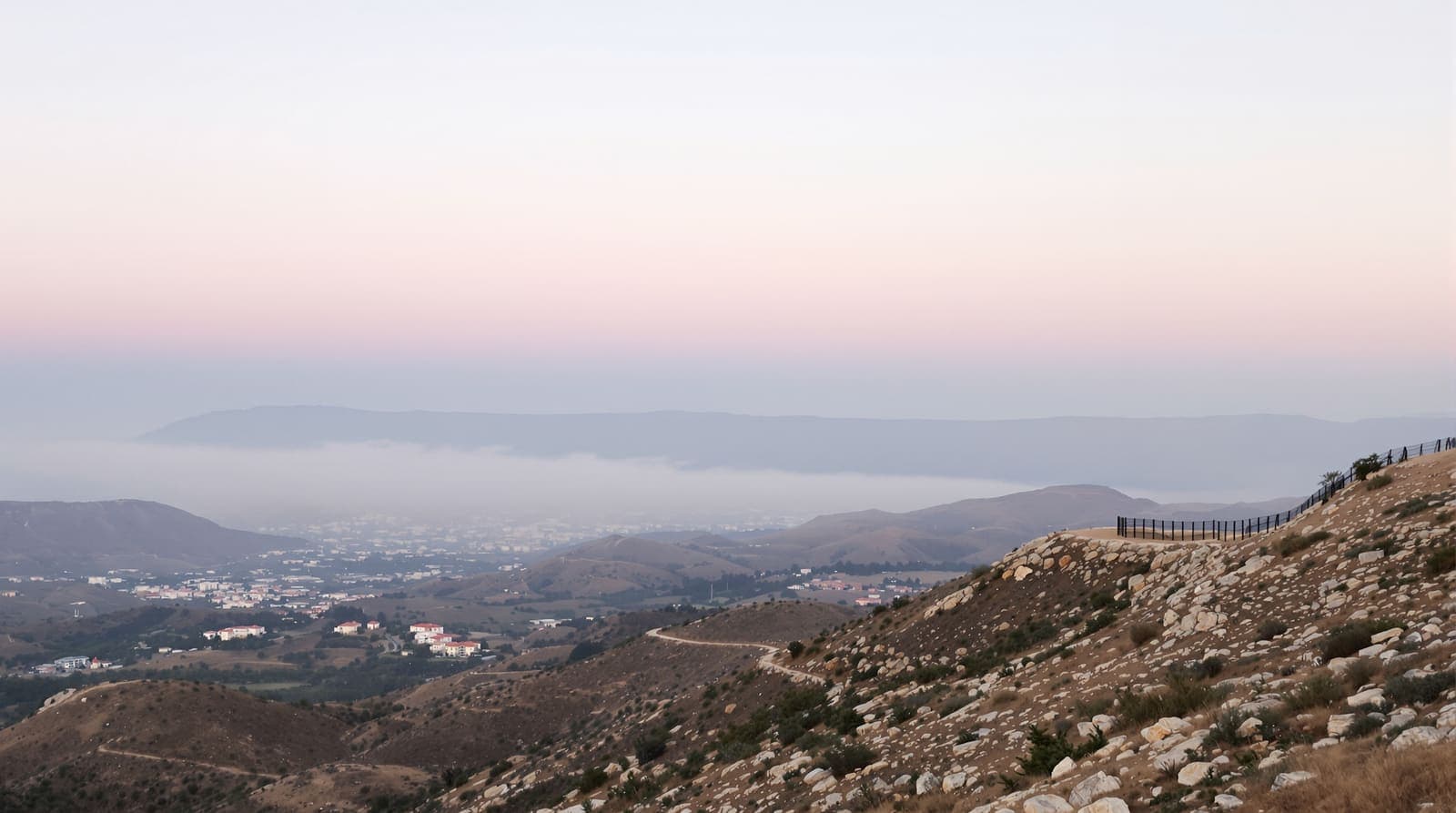 Illustration of terraced hills and distant stone villages in southern Lebanon seen from a border ridge at dawn, with haze over a far ridgeline.