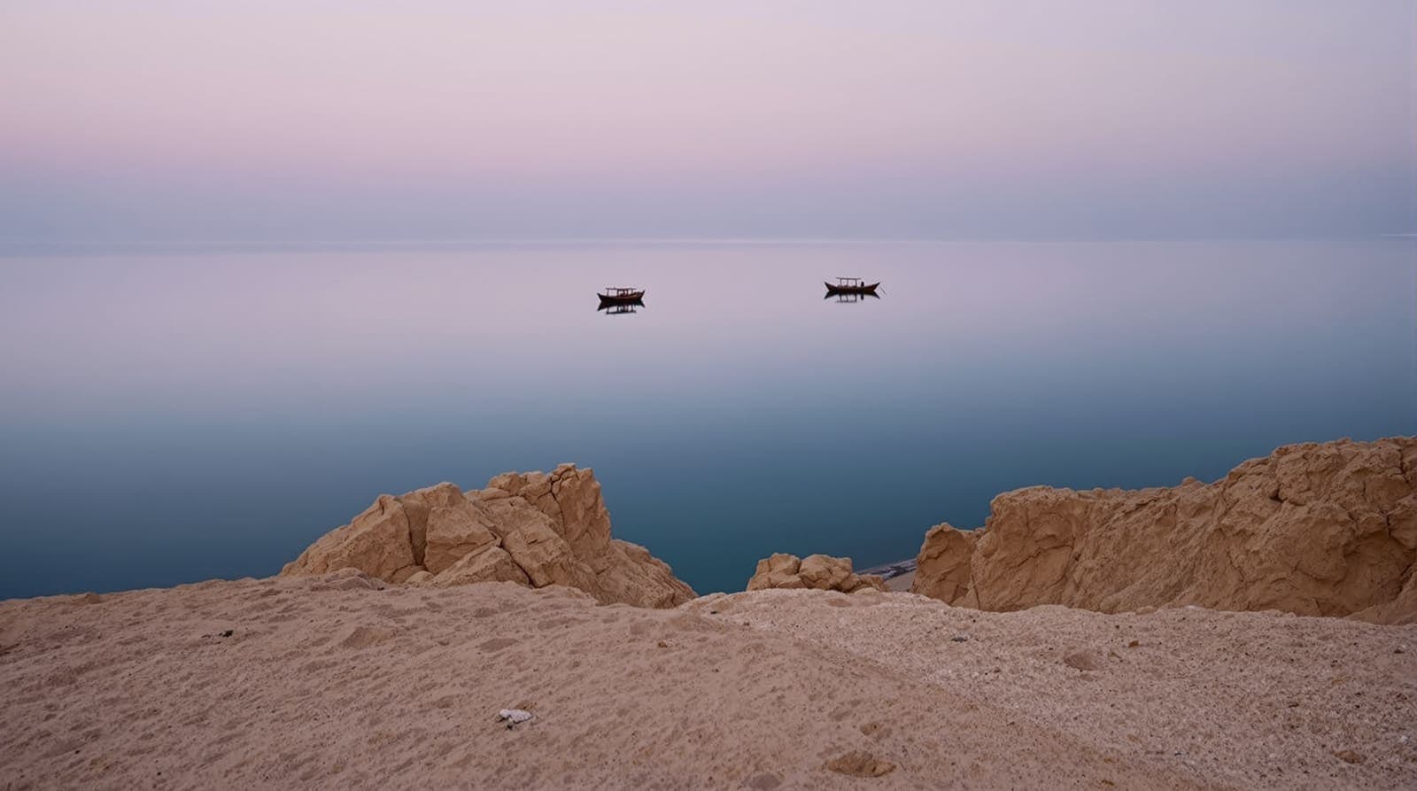 Illustration of two small fishing dhows silhouetted on calm water off Qeshm Island's arid cliffs at dawn