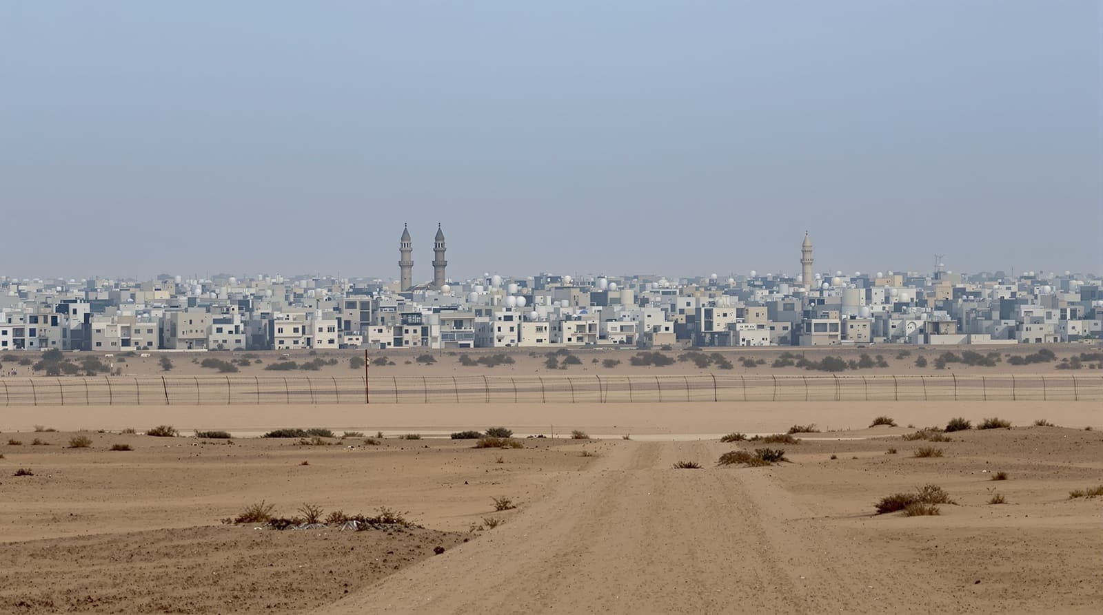 Illustration of the low, dense rooftops of Khan Younis seen at first light from across open fields on the Gaza perimeter.