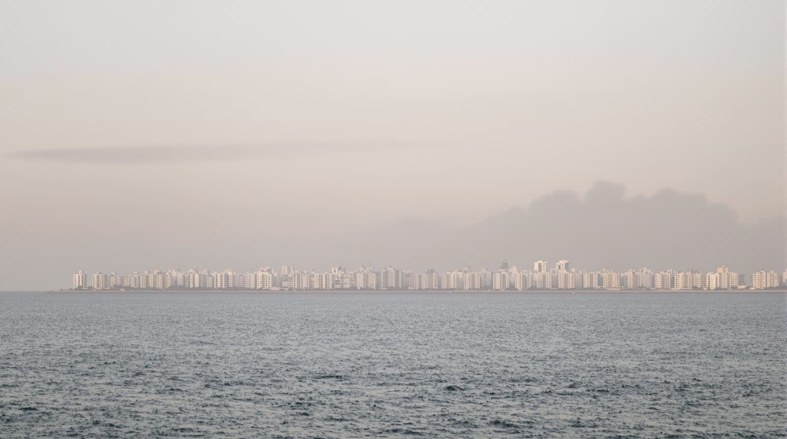 Illustration of the western Gaza City skyline along the Mediterranean shore, seen from a distance under hazy dawn light