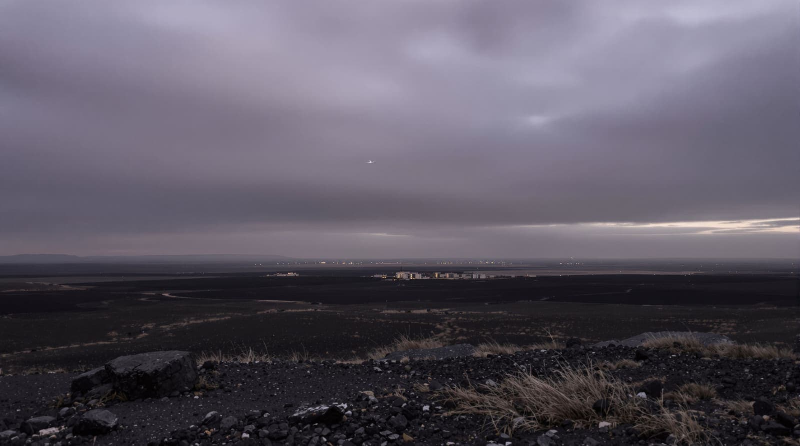 Illustration of the basalt plain and distant villages of southern Syria near Daraa under an overcast dusk sky with a faint contrail.