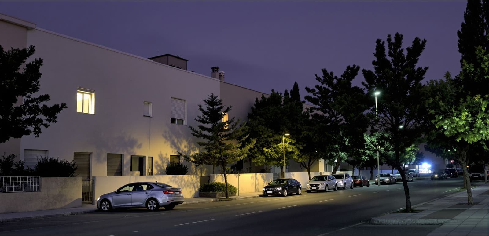Illustration of a quiet residential street of pale apartment blocks and trees in Yavne at dusk