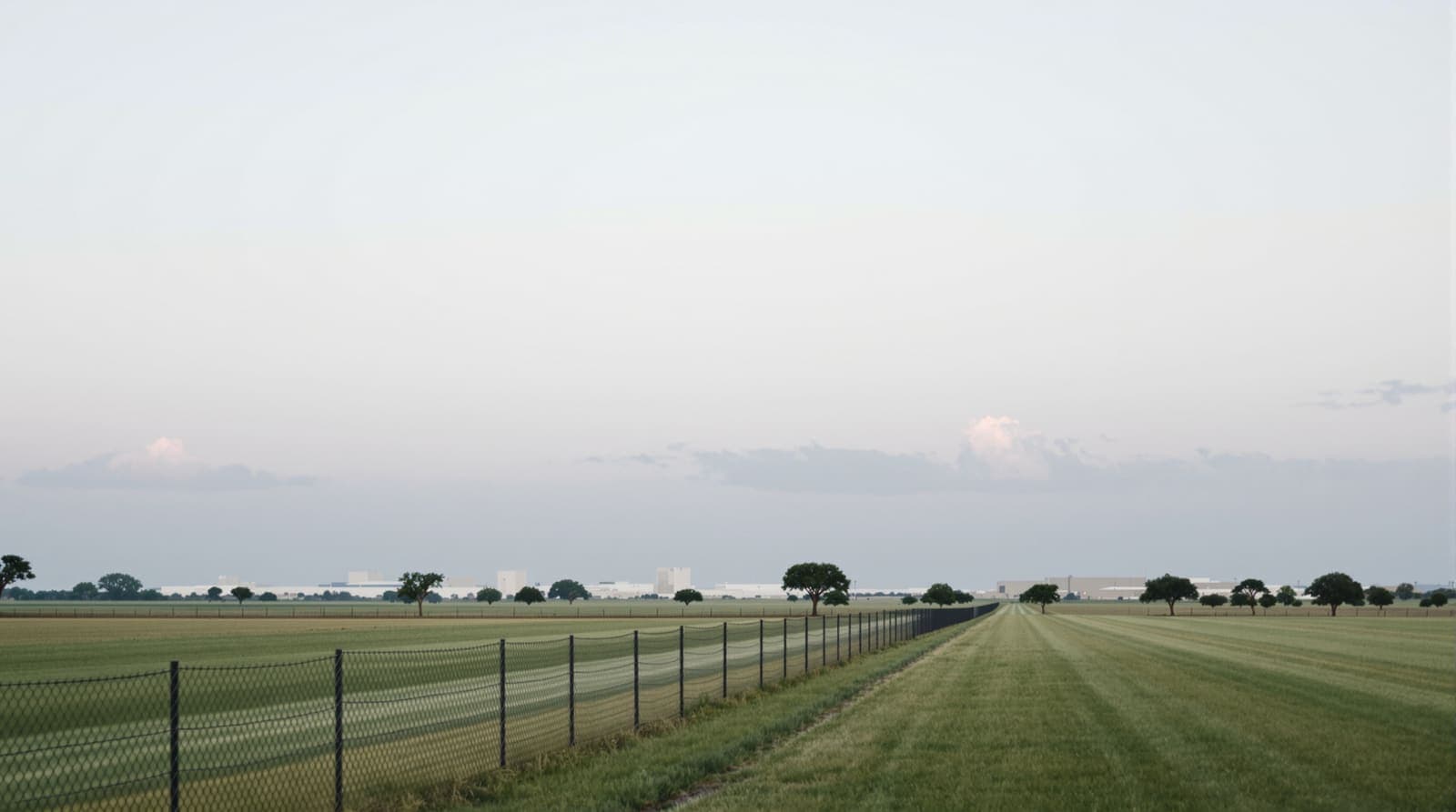 Illustration of a distant army base on flat Texas grassland at dawn, seen beyond a perimeter fence