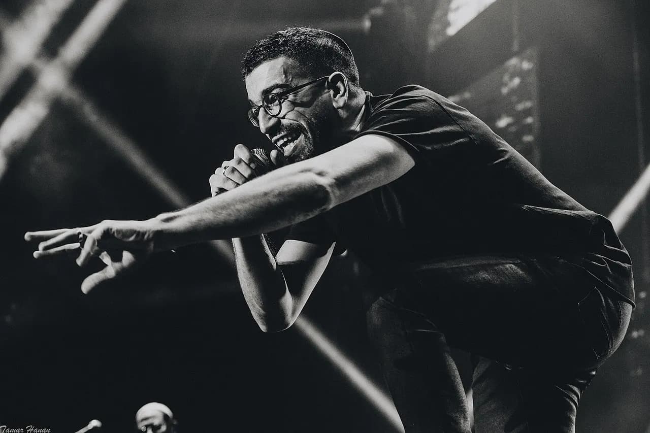 Hanan Ben Ari leaning toward the crowd with a microphone at Menora Mivtachim Arena, black and white, 2021
