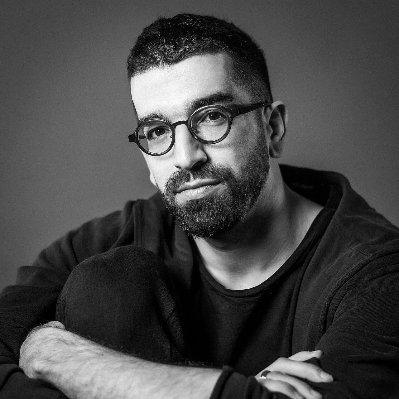Hanan Ben Ari sitting with his arms folded over one knee, a black and white portrait, 2022