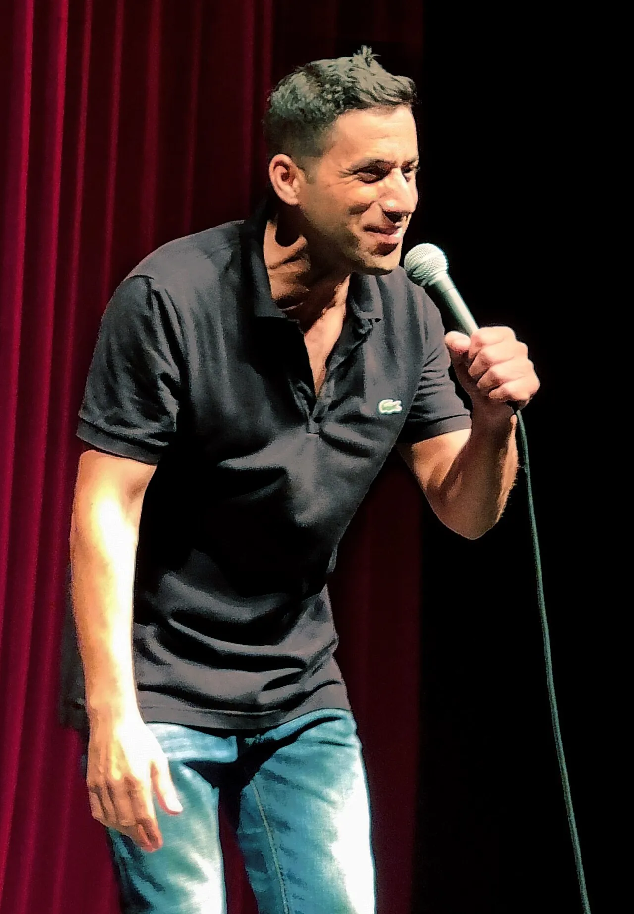 שחר חסון על הבמה עם מיקרופון, מול וילון אדום