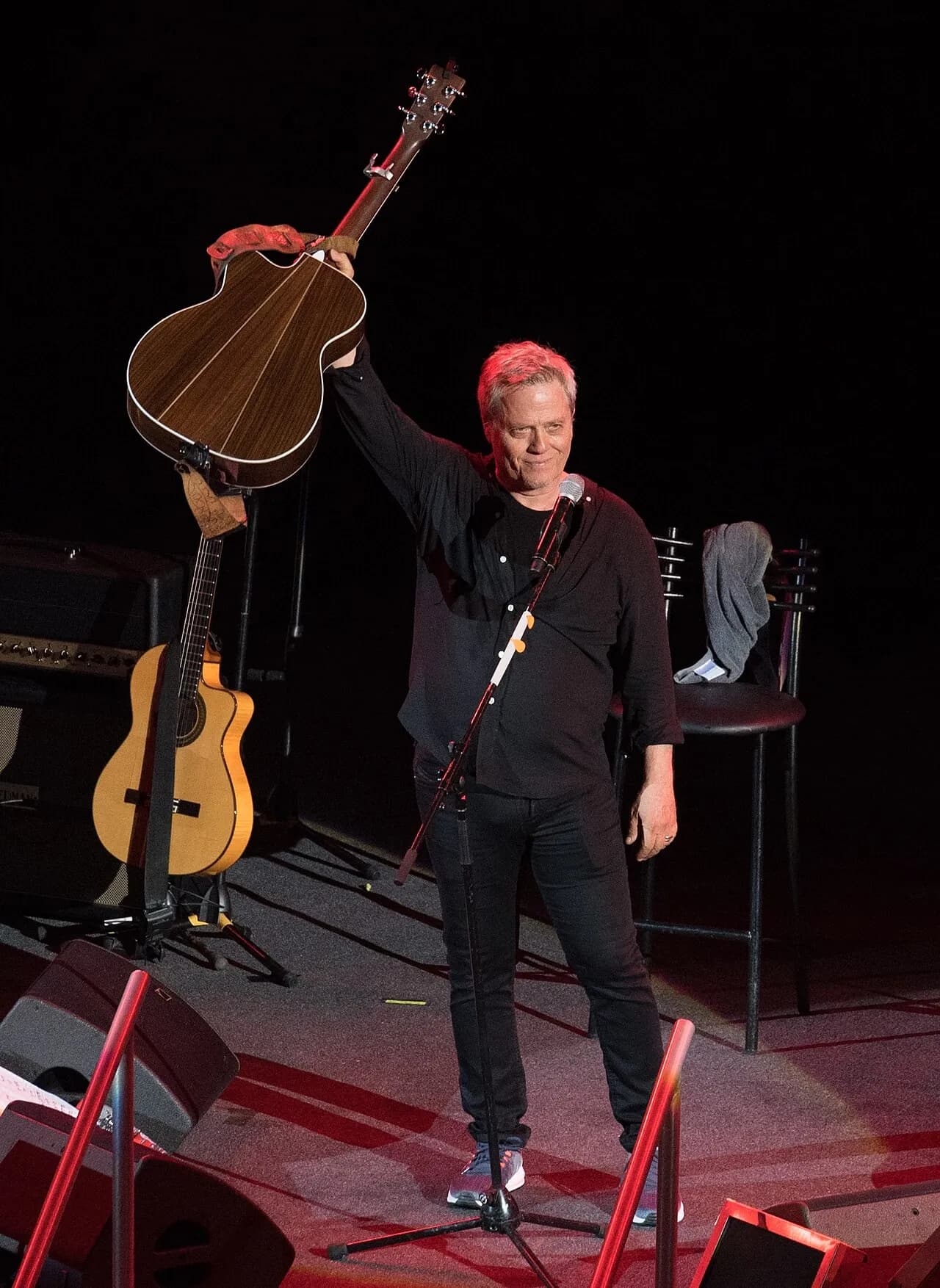 Shlomo Artzi on stage at Caesarea, raising an acoustic guitar to the crowd, 2018