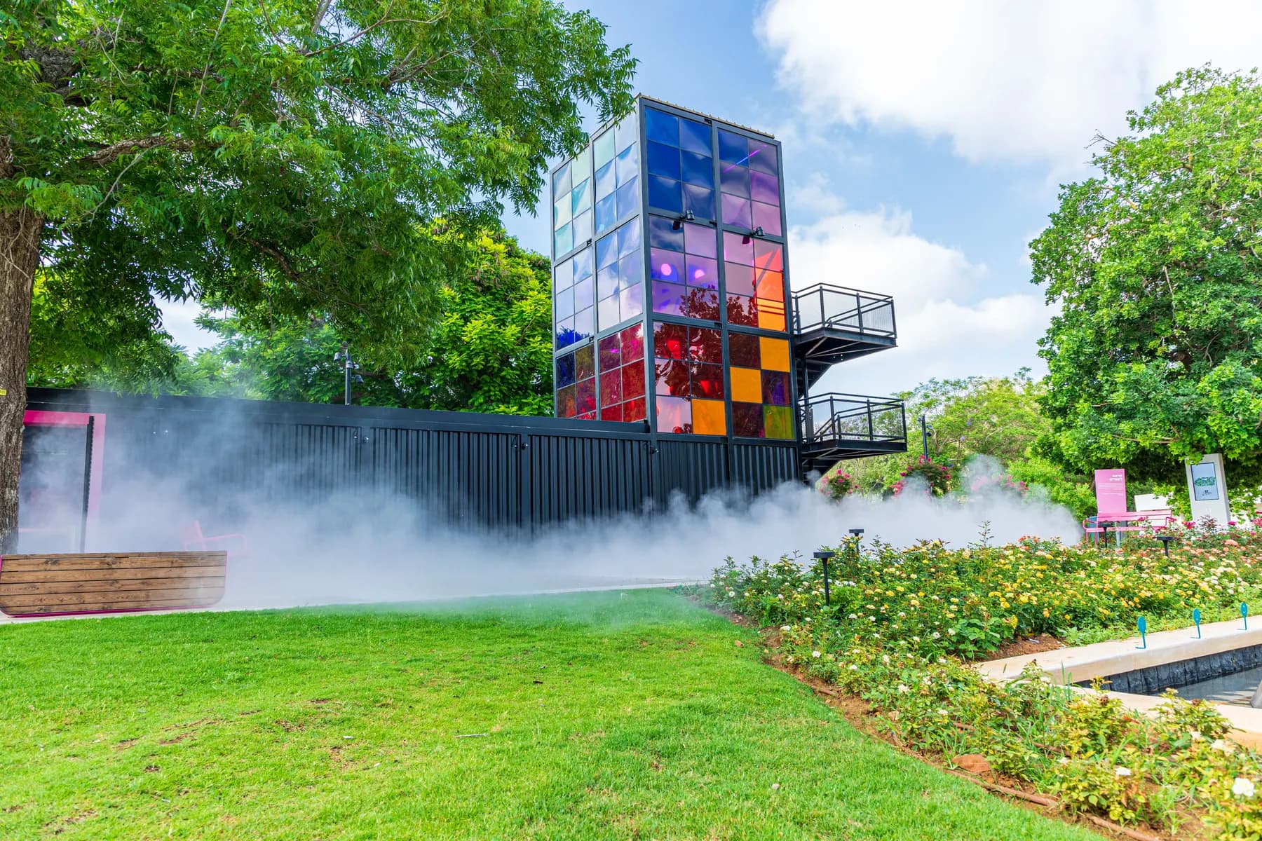 A tower of coloured glass panels above a lawn and a mist of water at the Clore Garden of Science