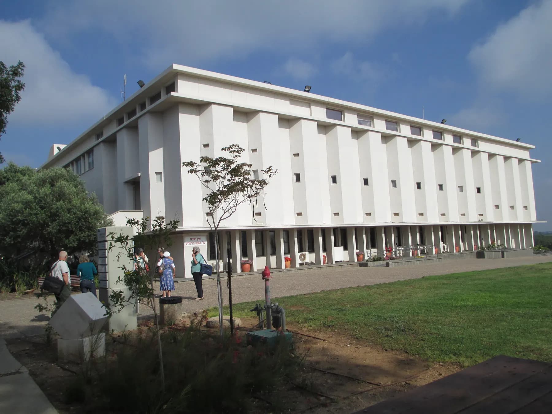 המבנה הלבן והארוך של בית לוחמי הגטאות, ומבקרים על הדשא שלפניו