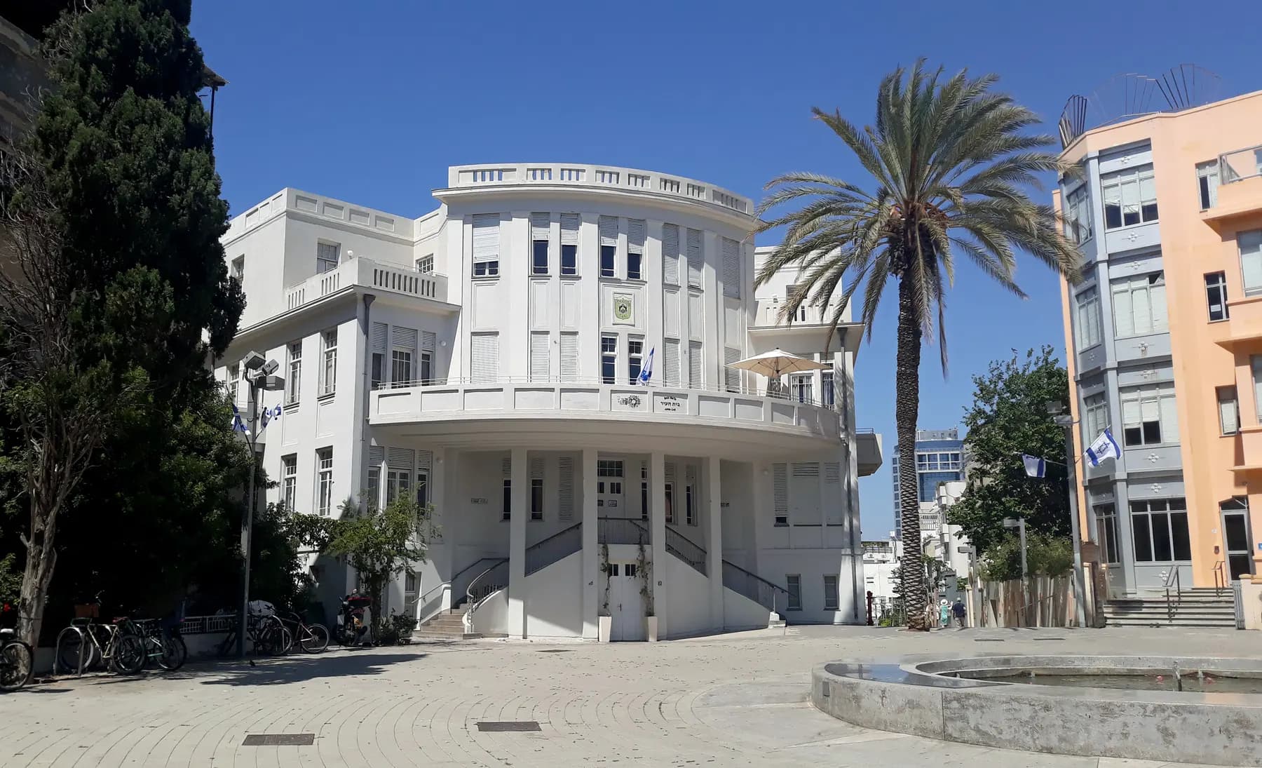 Beit Ha'ir's white building on Bialik Square, with palm trees beside it