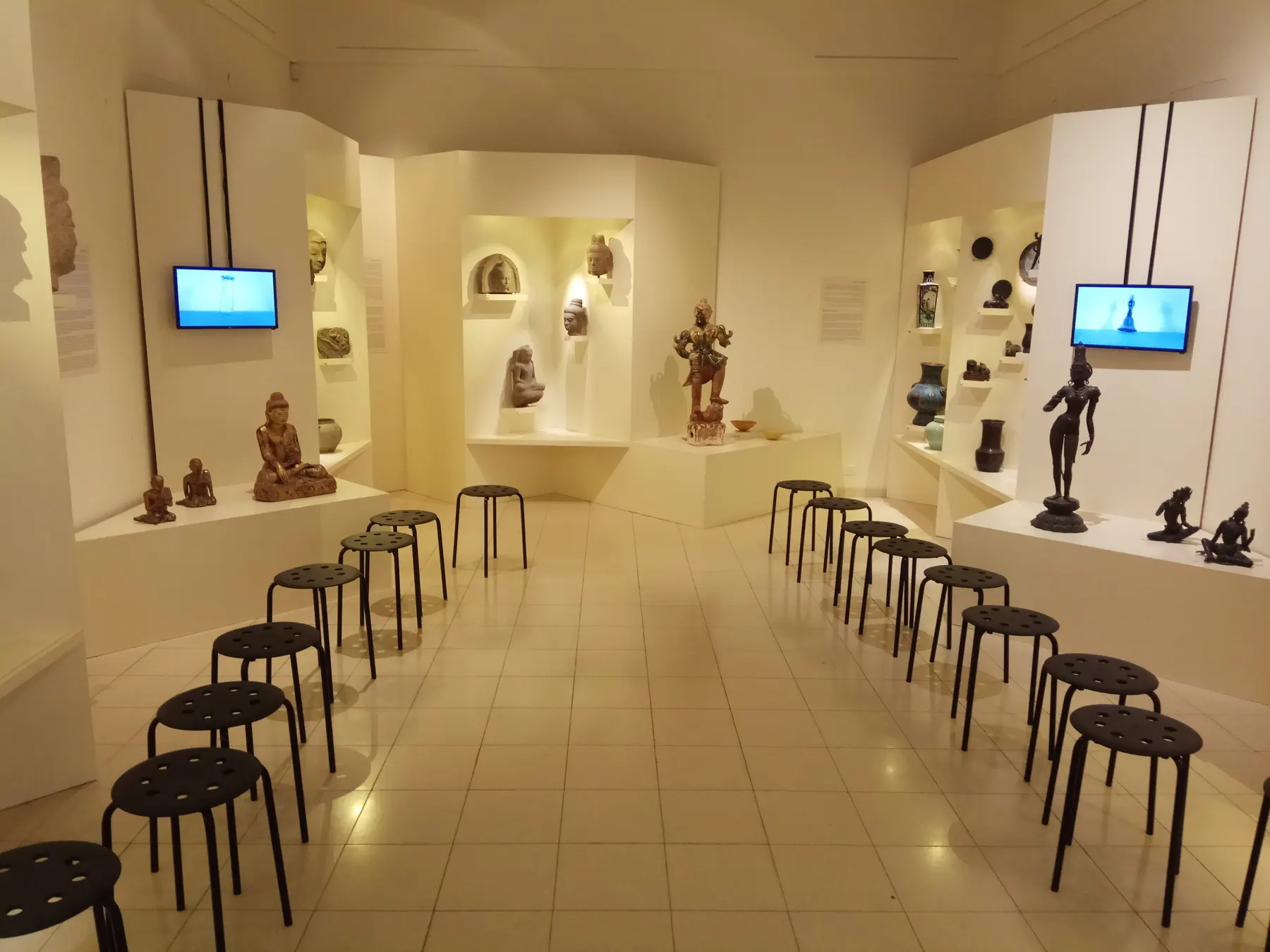 A hall of the Wilfrid Israel Museum at HaZorea, with figures and objects in lit niches and rows of stools
