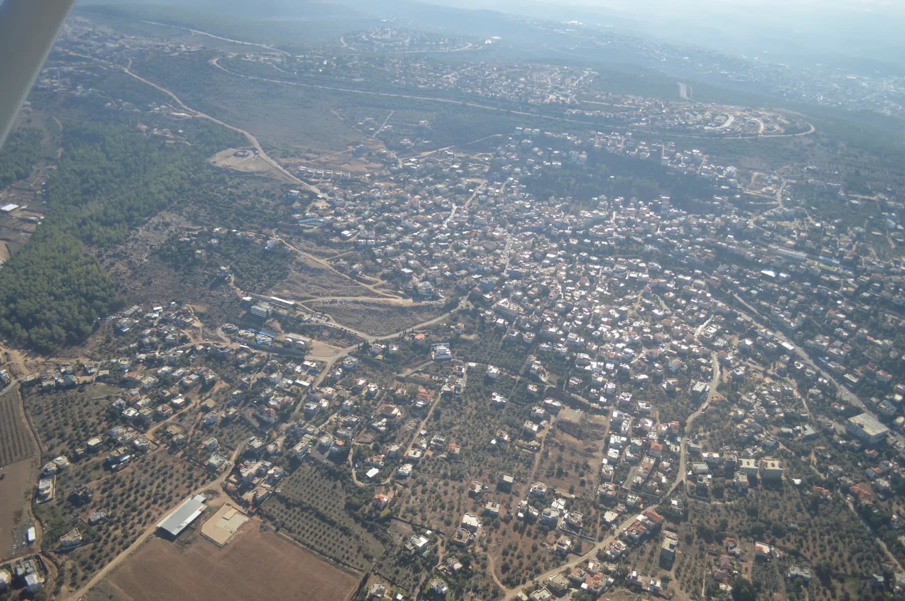 An aerial view of Arara, with houses spread over the hills among olive groves and pine woods.