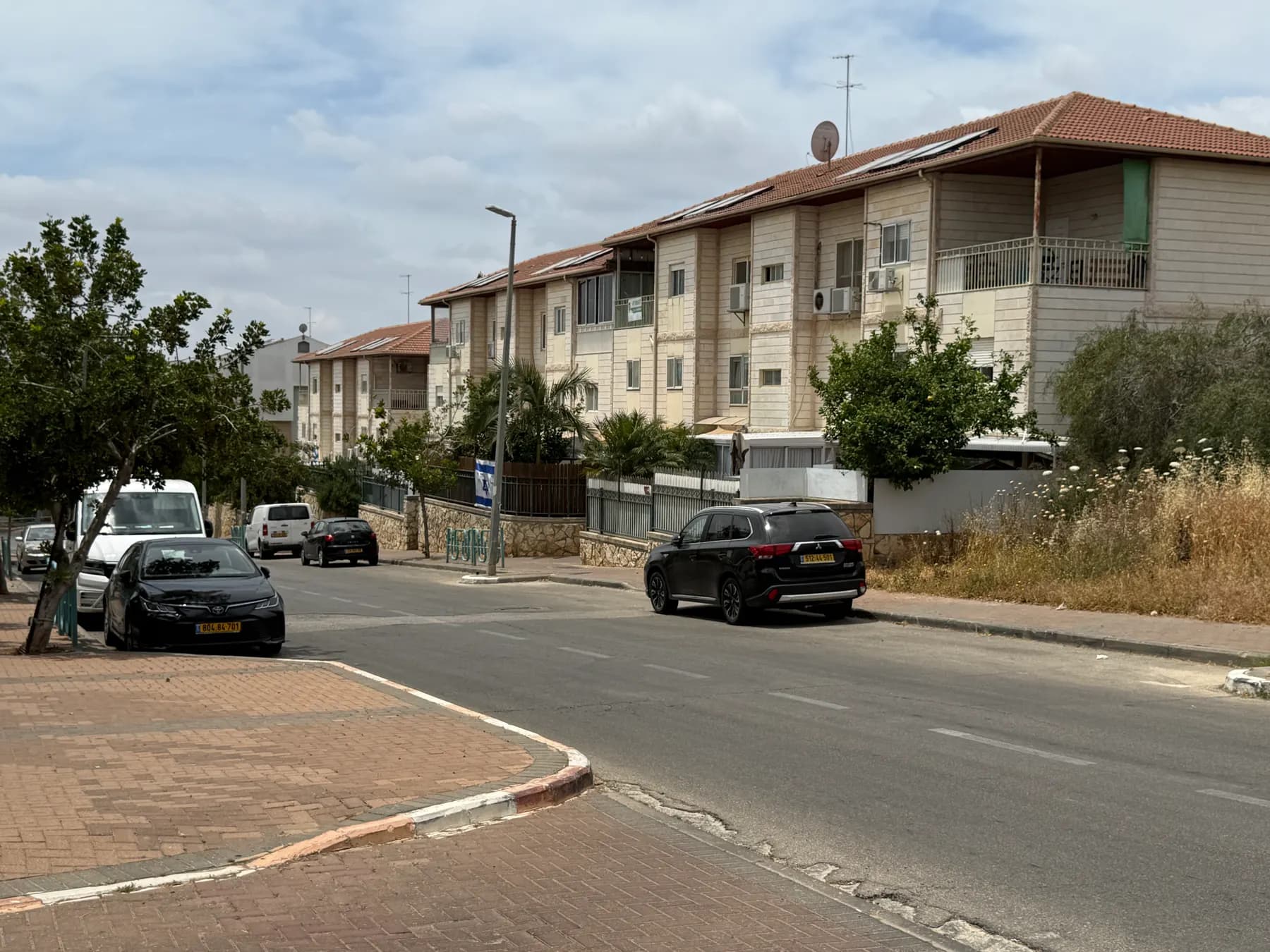 A street in Ariel lined with three-storey apartment buildings, trees and parked cars.