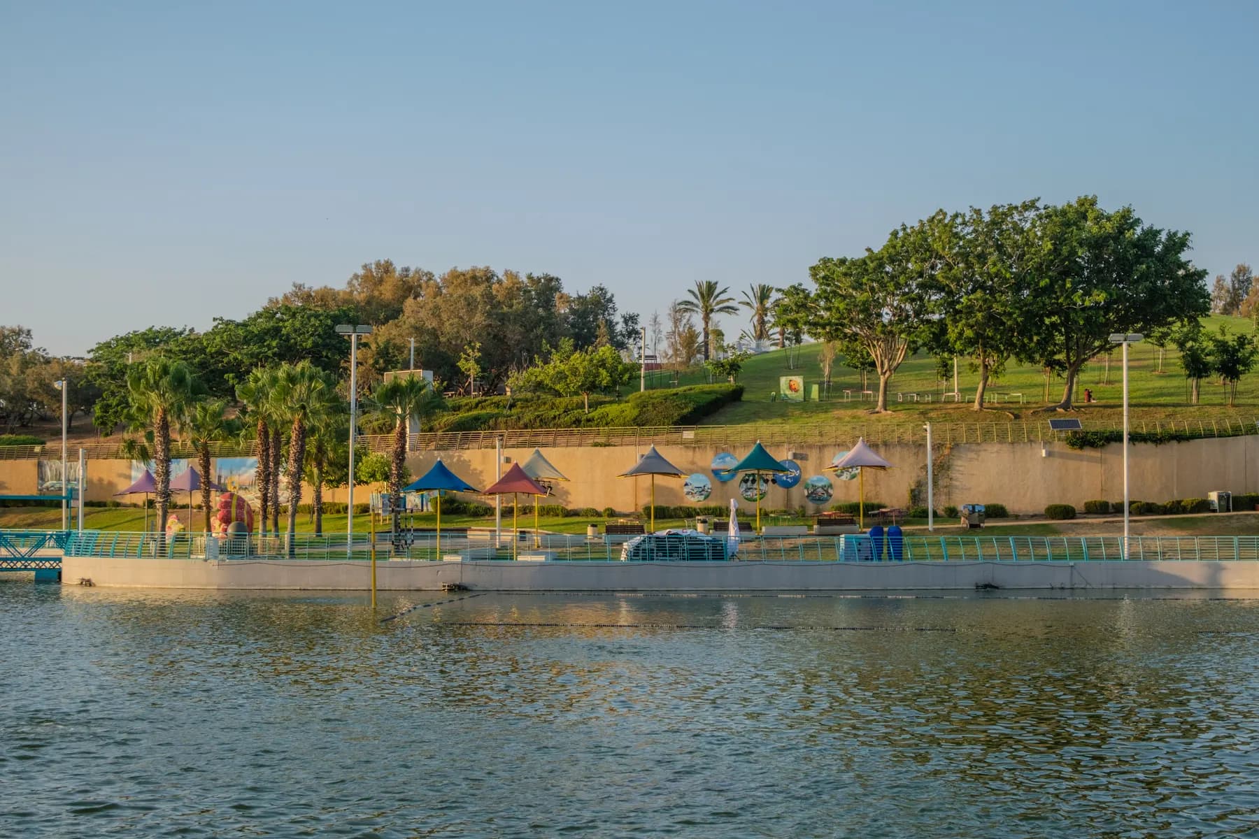 The lake at the centre of Ashdod Yam Park before sunset, with lawns, trees and shaded picnic spots on its far bank