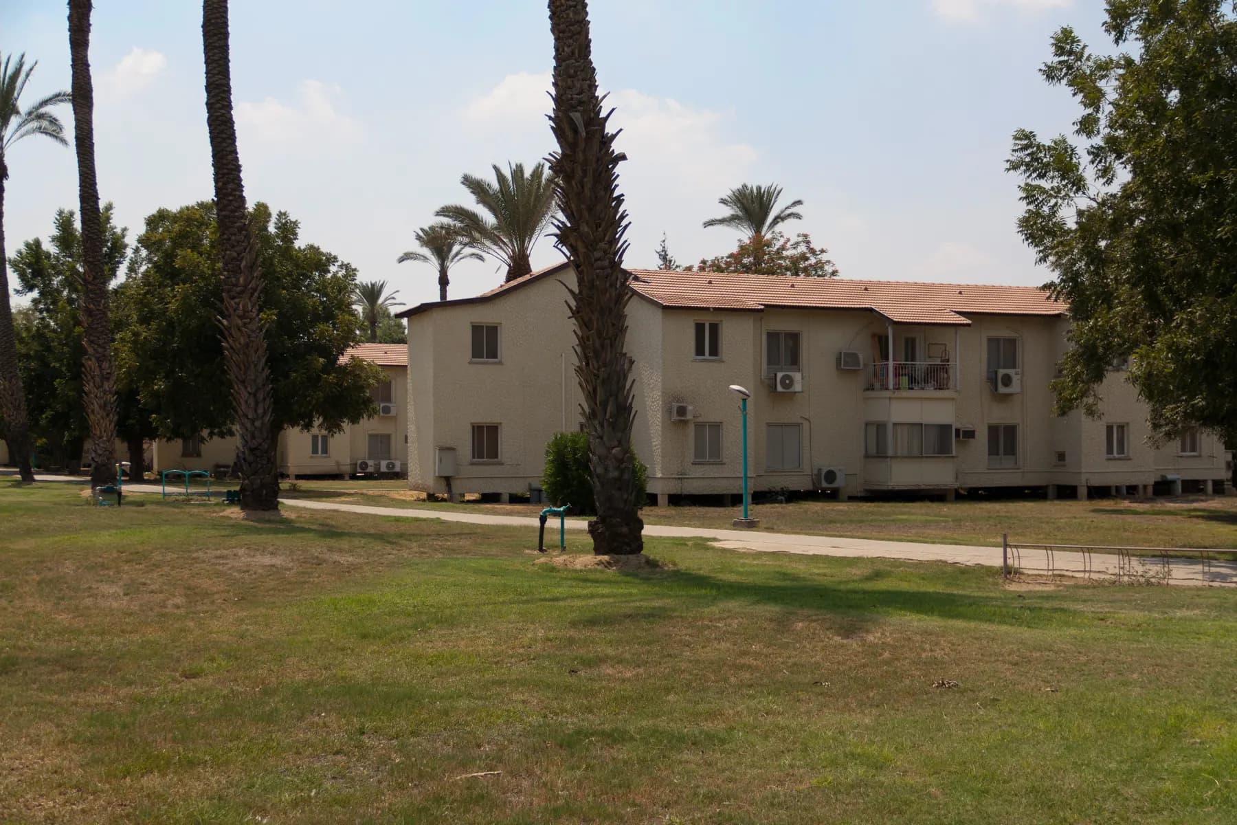 A two-storey residential building among palm trees beside a lawn and a footpath in Ashdot Ya'akov Meuhad.