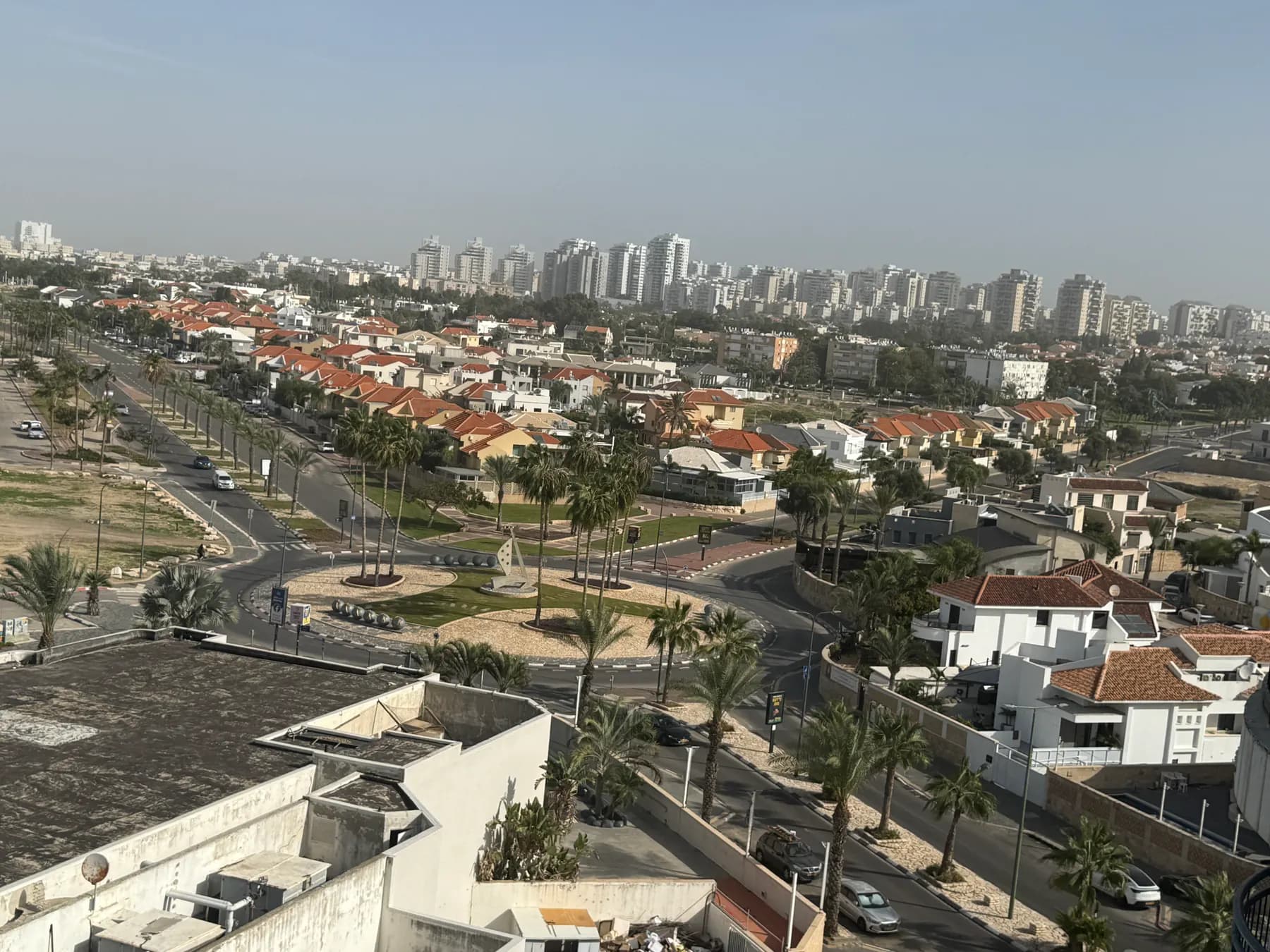 Red-roofed houses and palm-lined streets in Ashkelon seen from above, with apartment towers behind.
