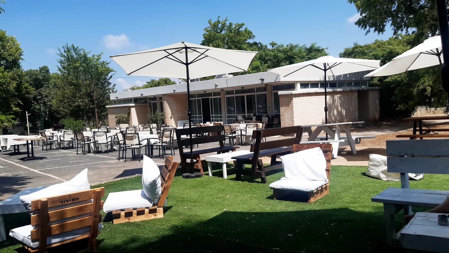 Outdoor tables, benches and white parasols on a lawn in front of a long, low building in Bahan.