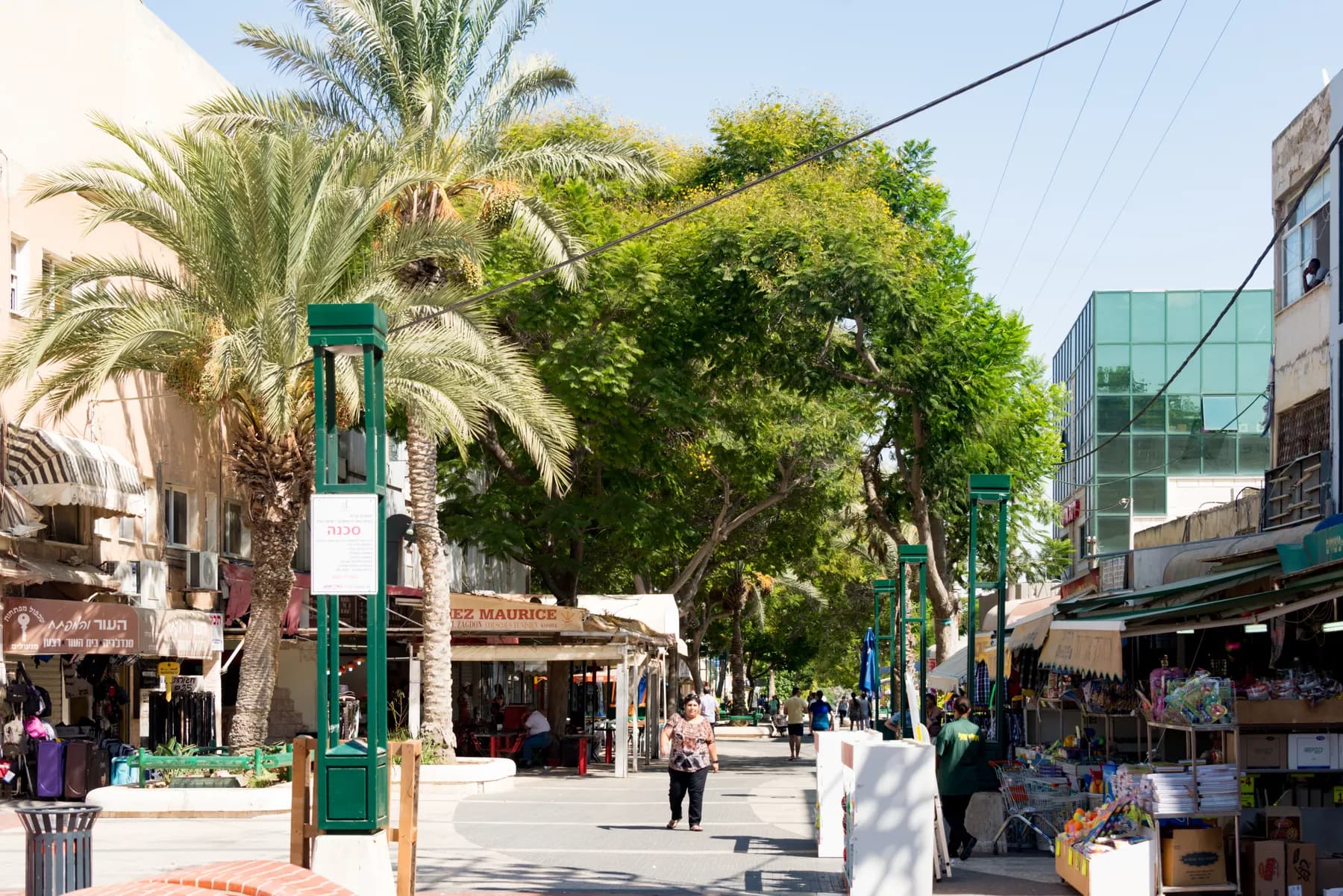 A tree-lined pedestrian street in the centre of Beer Sheva, with palm trees, shop awnings and café tables