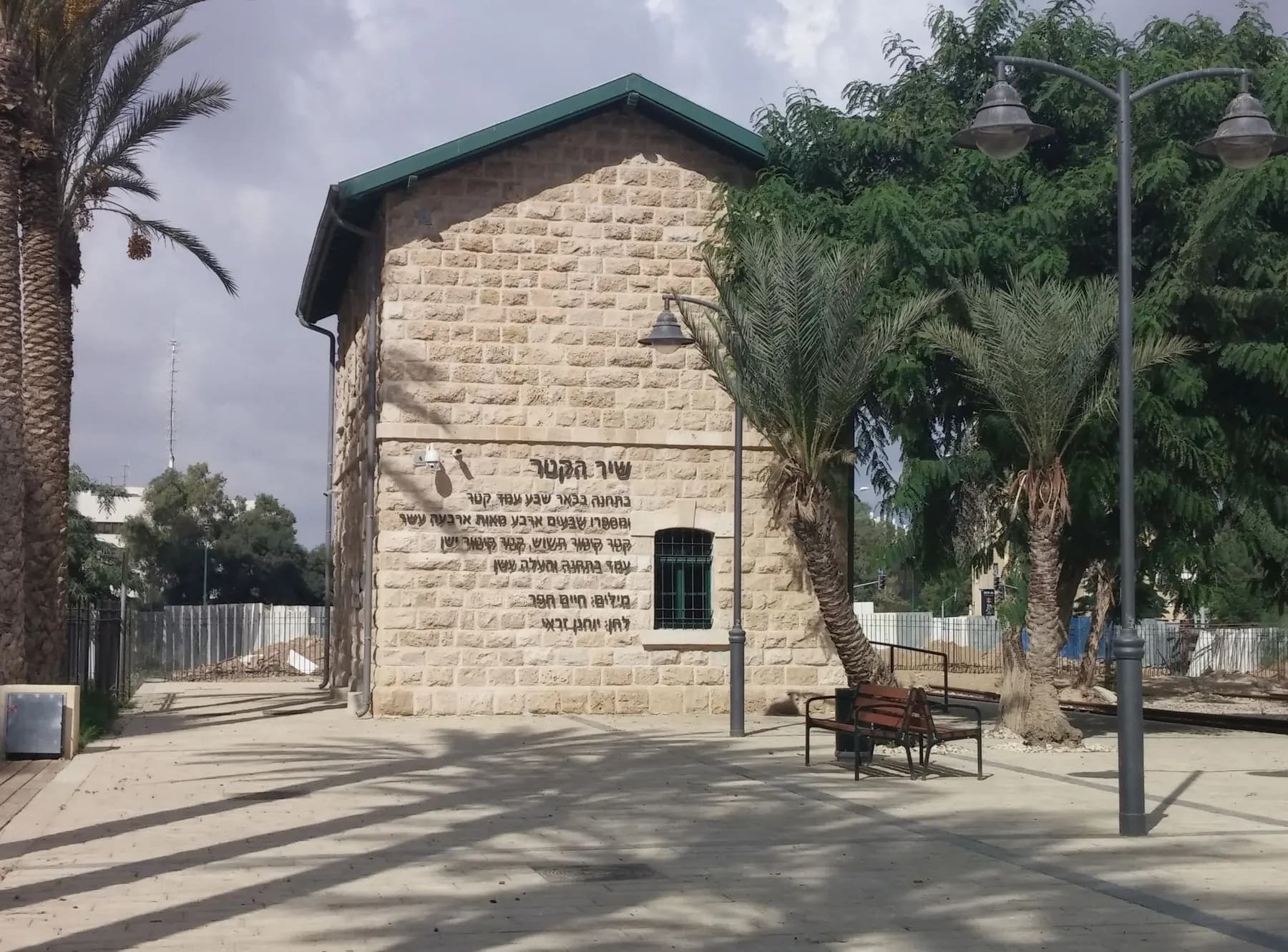 The stone building of Beer Sheva's restored Ottoman railway station, with palm trees and a lamp post beside it
