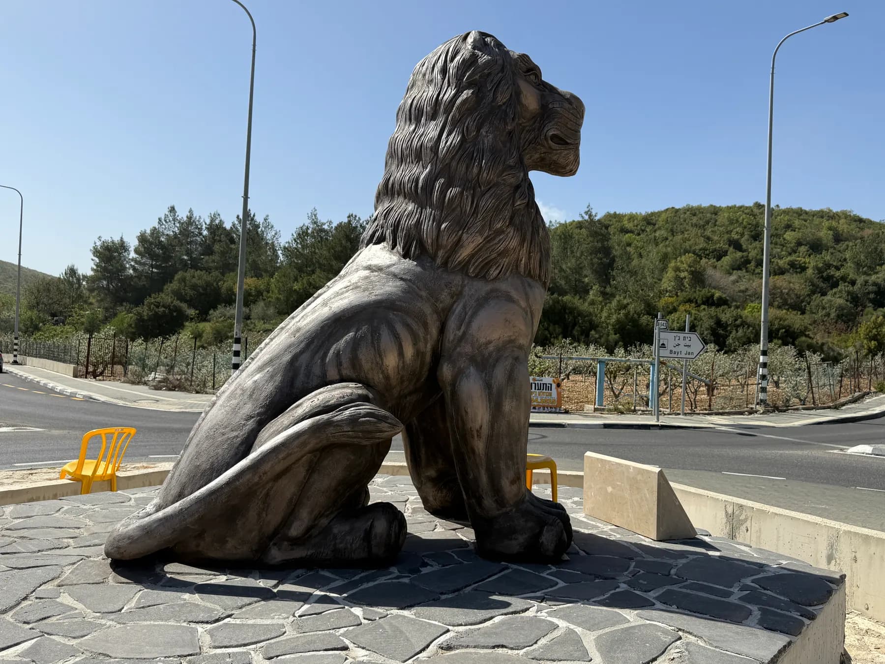 A large lion statue on a stone base at the Beit Jann junction, with wooded hills behind.