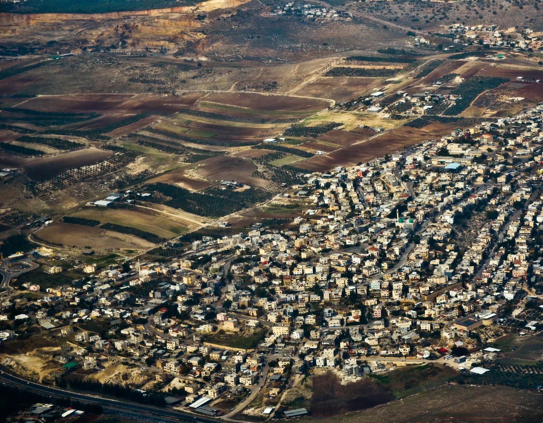 An aerial view of the houses of Bir al-Maksur packed on a hillside, with farm fields beyond.