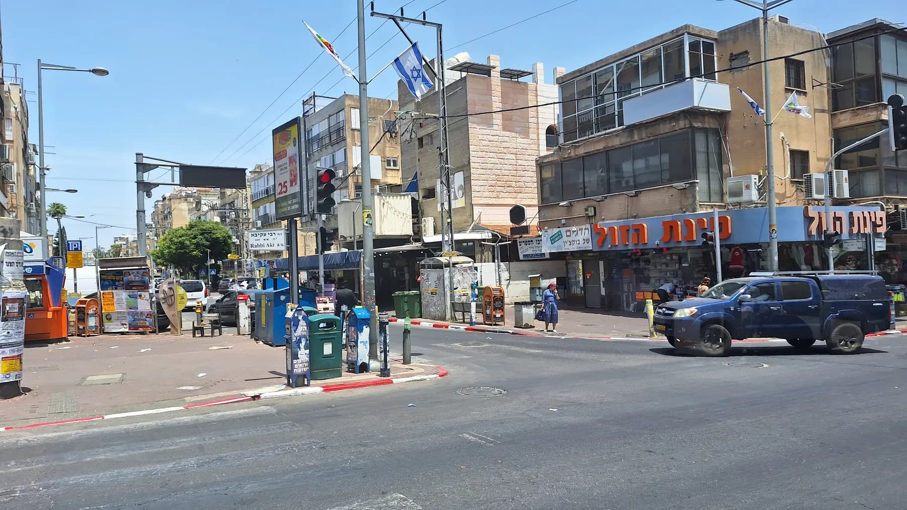 A street junction in Bnei Brak with shops on the ground floors, traffic lights and an Israeli flag.
