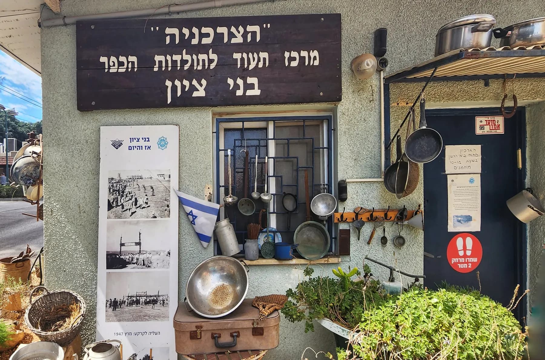 The front of the village history centre in Bnei Zion, hung with old pots, pans and photographs under a wooden sign.