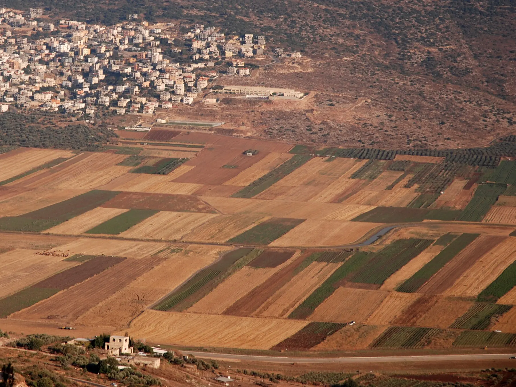 Houses of Bu'eine Nujeidat on a hillside above a patchwork of farm fields in the valley.