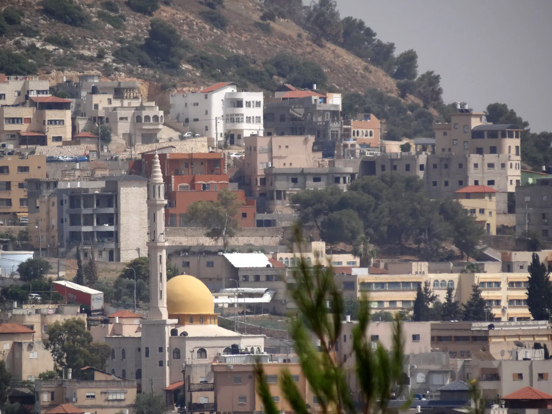 Houses of Daburiyya on a hillside, with a mosque with a golden dome and a tall minaret among them.