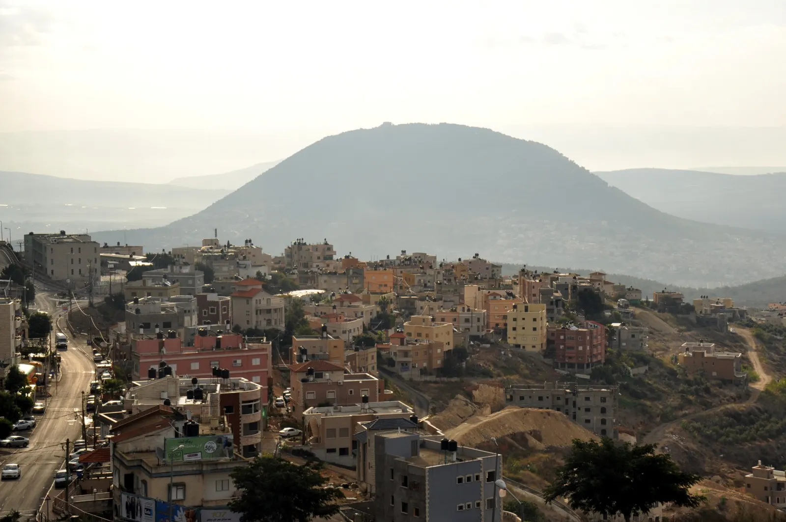 Houses of Ein Mahil along a hillside road, with a rounded mountain rising behind in the haze.