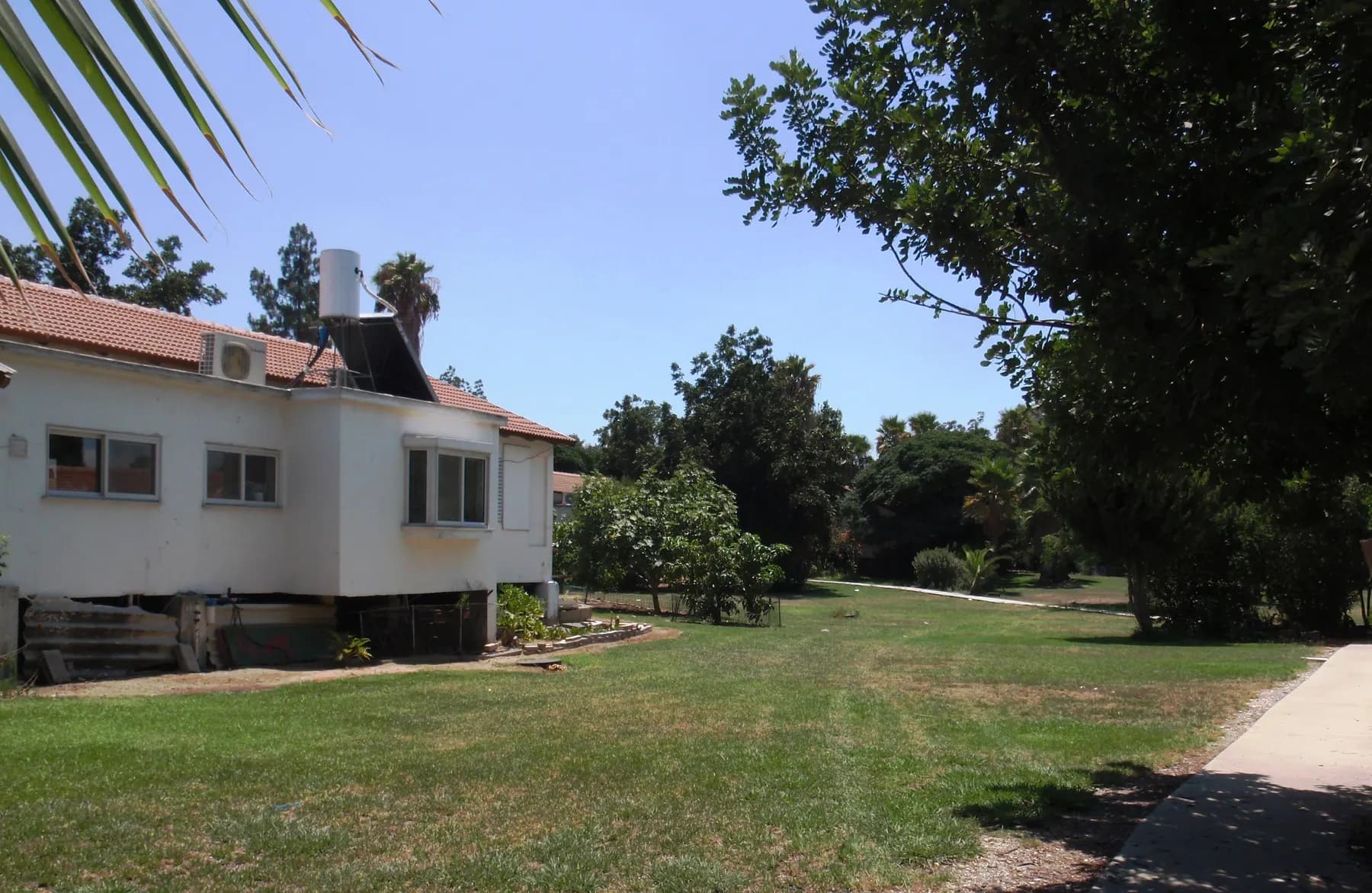 A white house with a red tiled roof beside a wide lawn and shade trees inside Kibbutz Einat.