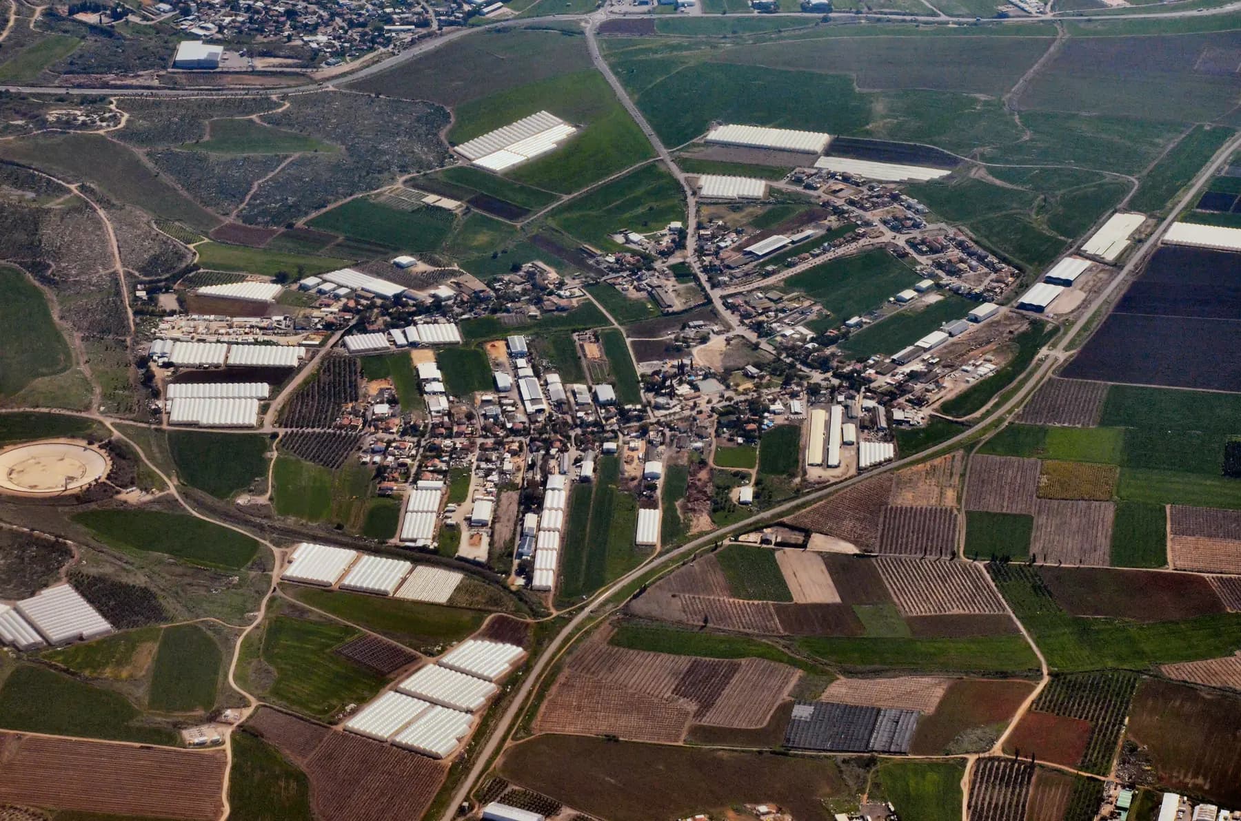 An aerial view of Giv'at Ko'ah, with houses and farm buildings spread among greenhouses and fields.