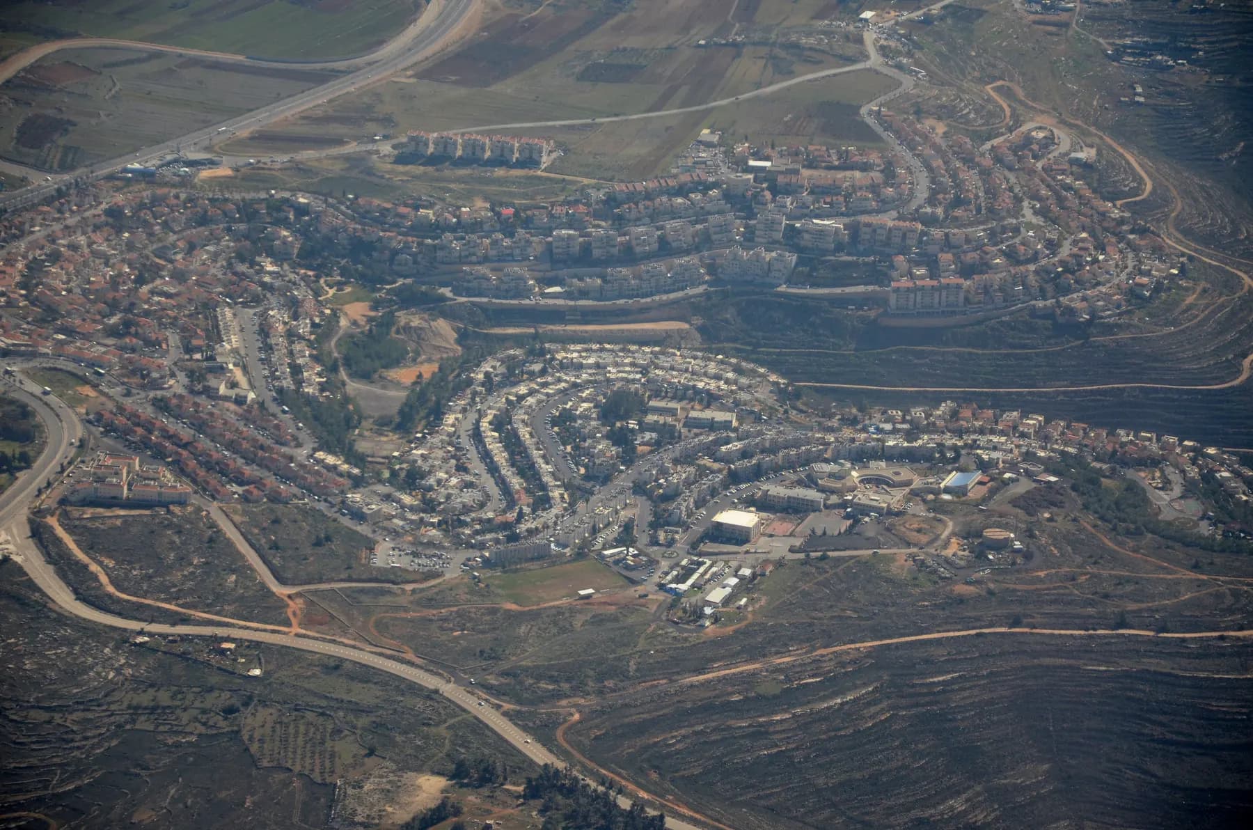An aerial view of Givat Ze'ev, with curving rows of apartment buildings along a hillside and roads winding around them.