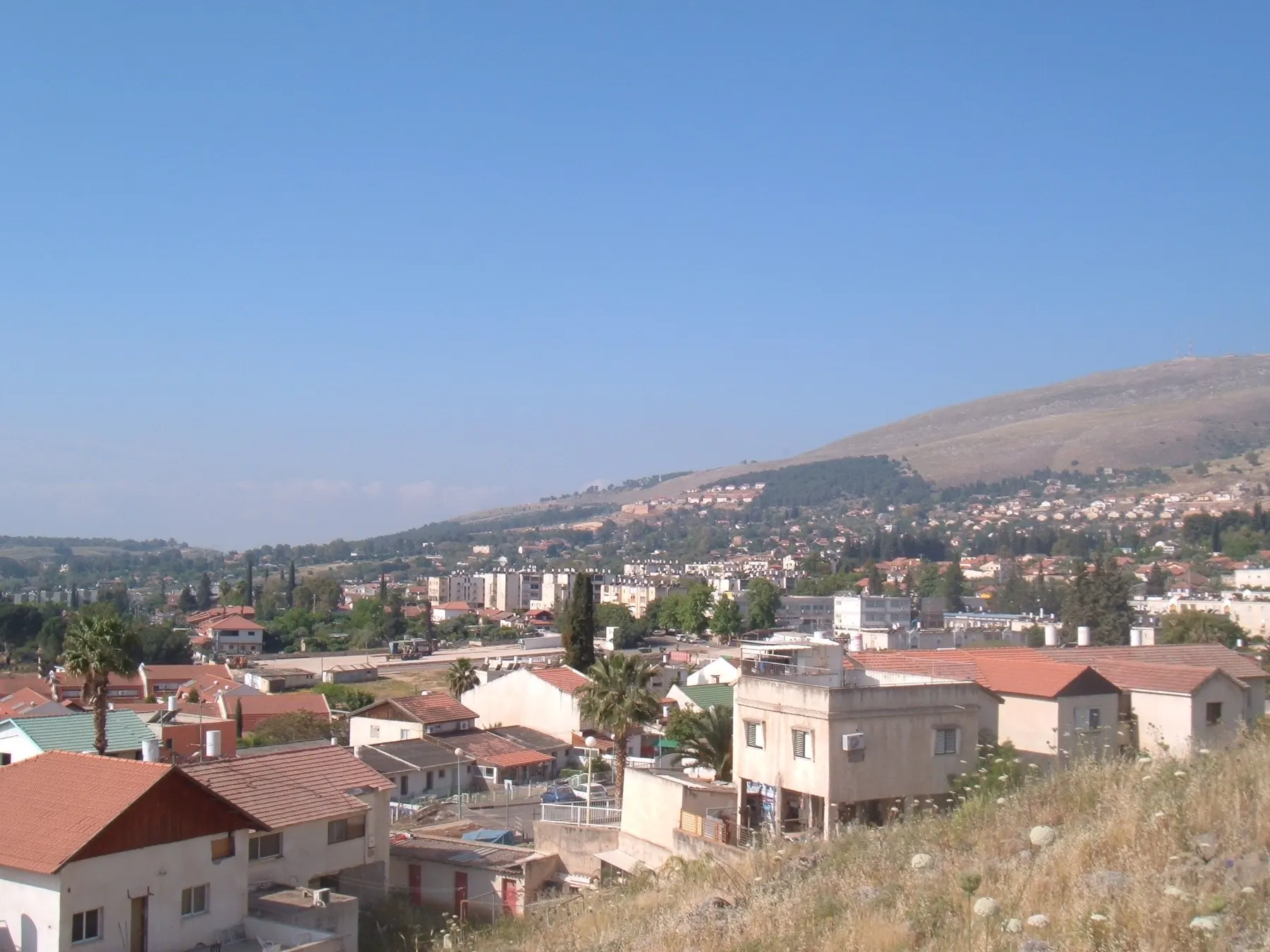 Red-roofed houses and apartment blocks in Hatzor HaGlilit, with a hillside rising behind.