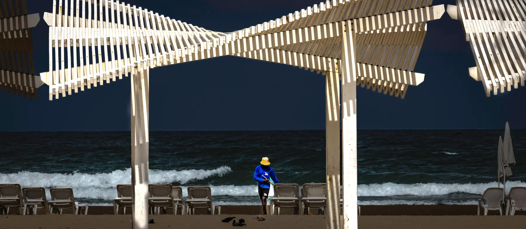 A white wooden pergola on Arena beach in Herzliya Pituach, with the sea behind it