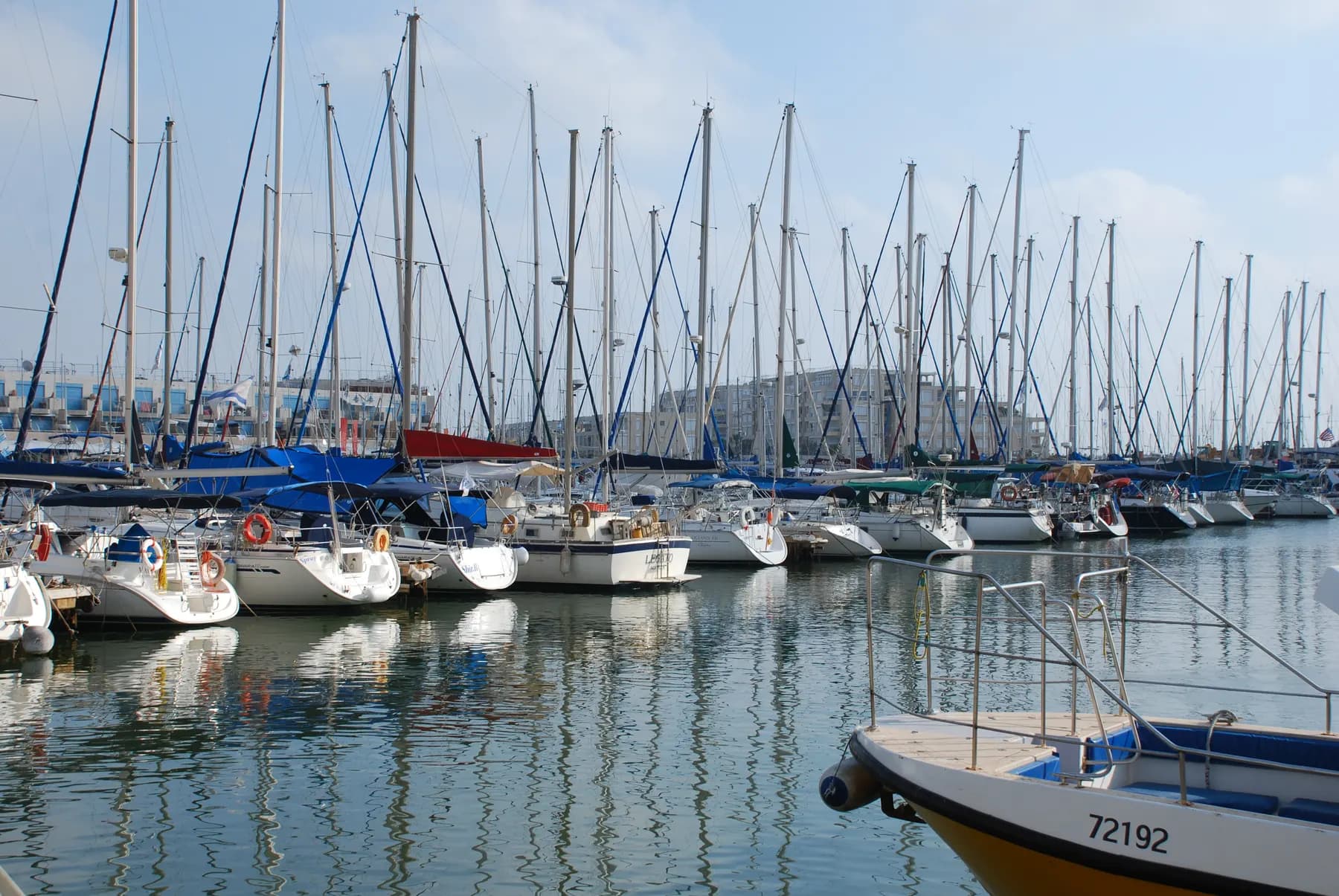 Sailing yachts moored in Herzliya Marina, with the buildings around the marina behind them