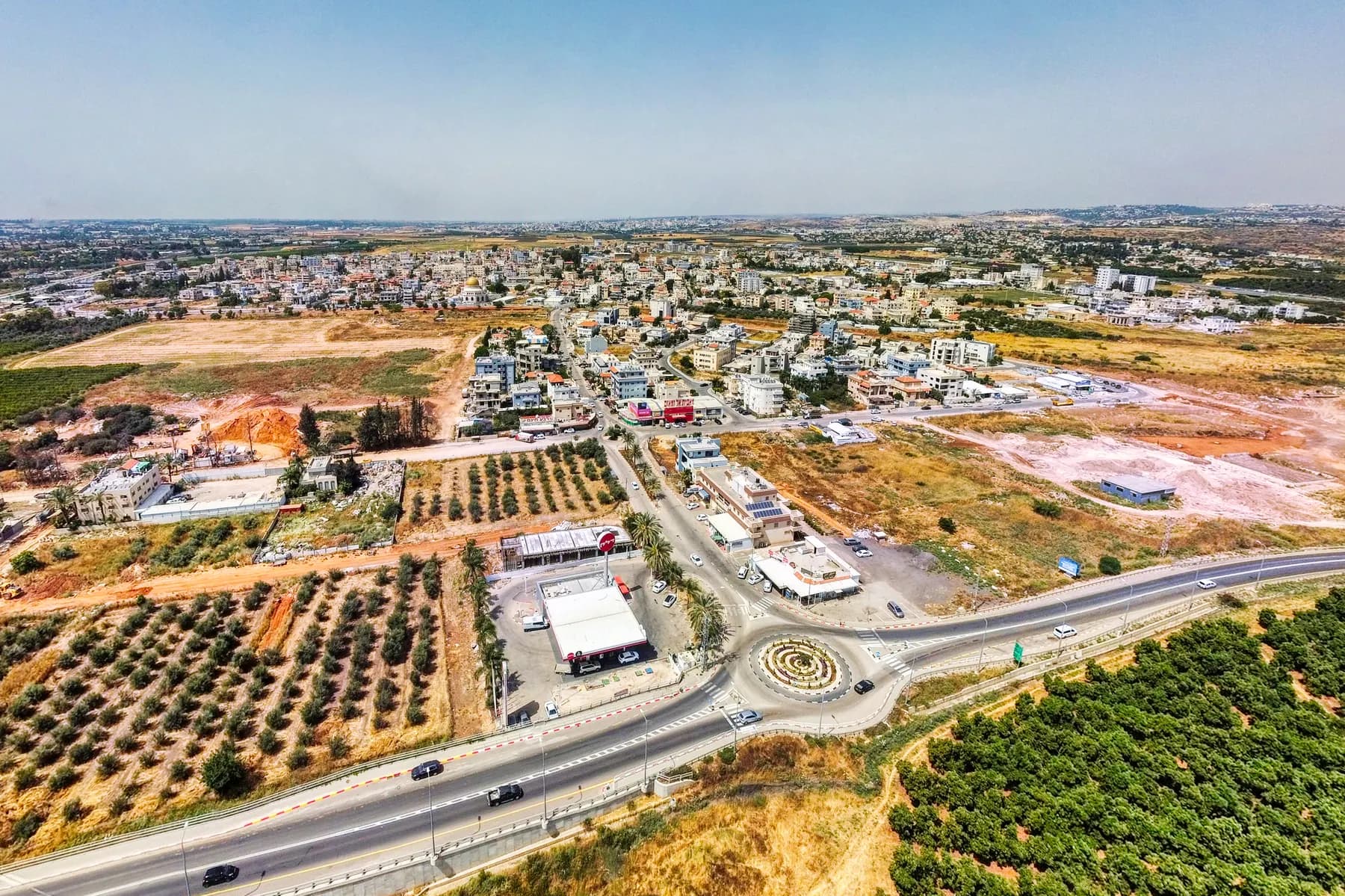 An aerial view of Jaljulia, with a roundabout and a main road in front of the town and olive groves beside it.