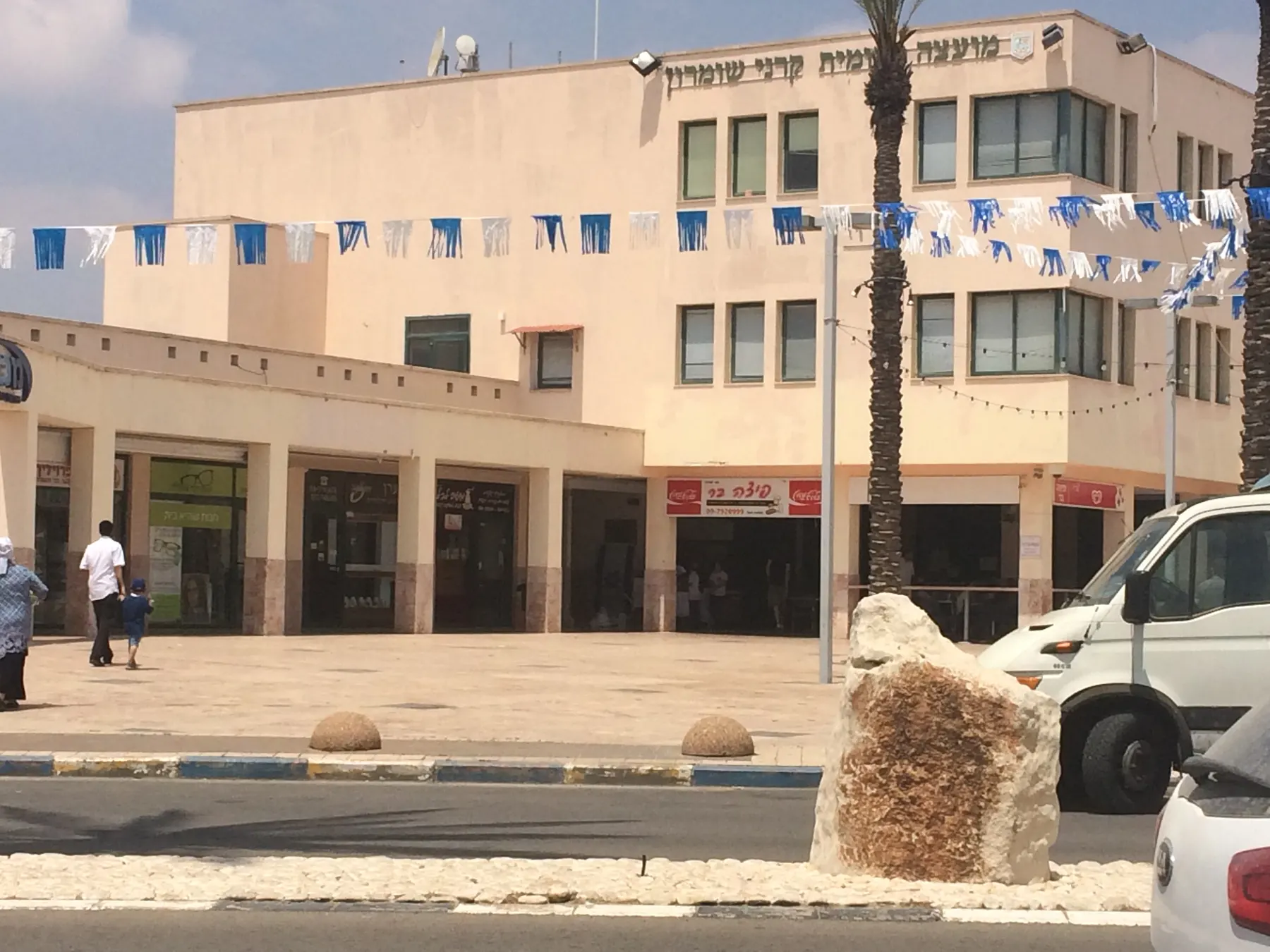 The Karnei Shomron mall, with shops under an arcade and strings of blue and white flags across the square.