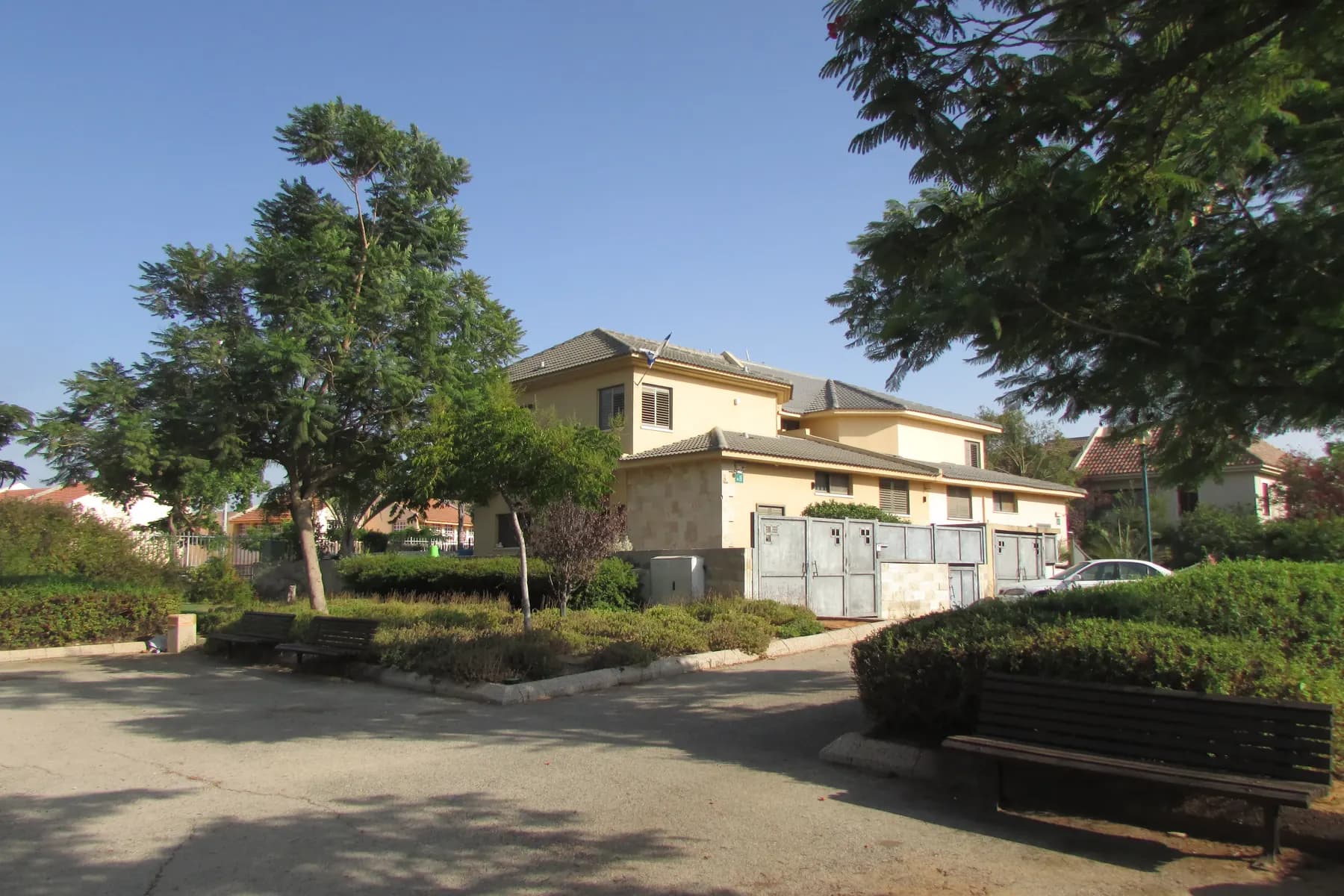 A two-storey house beside a small park with benches and trees in the Kaplan neighbourhood of Kfar Saba.