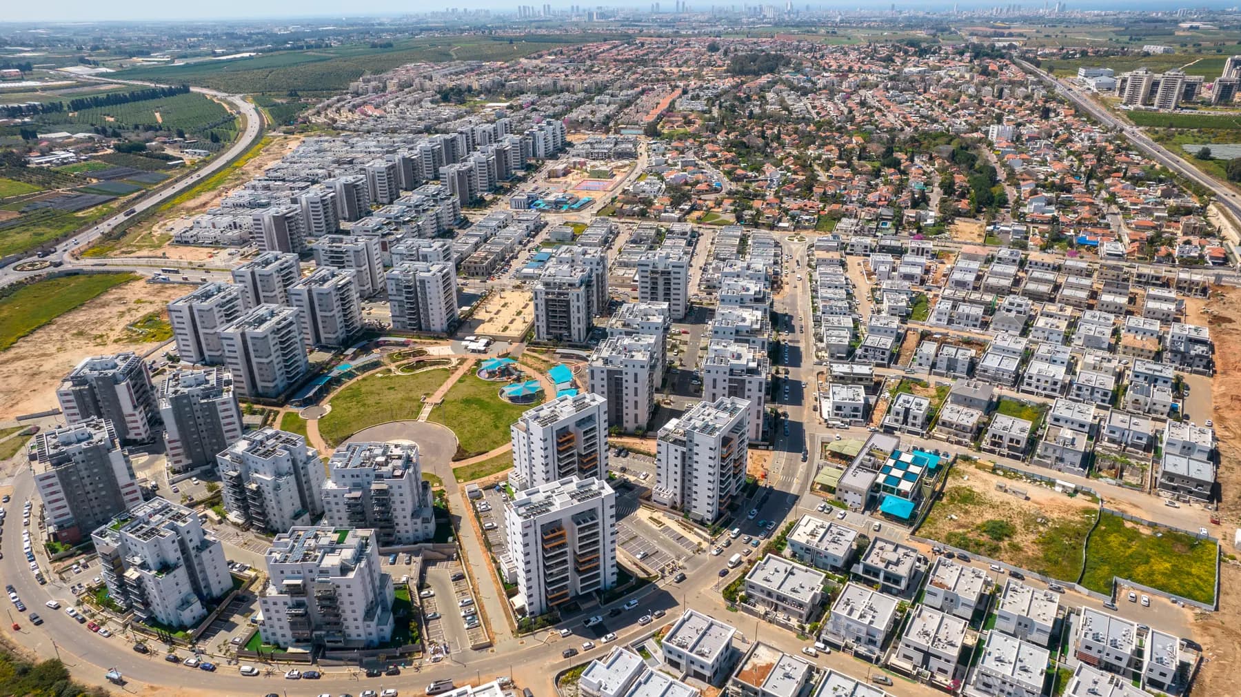 An aerial view of Kfar Yona, with new apartment towers around a green park and red-roofed neighbourhoods beyond.