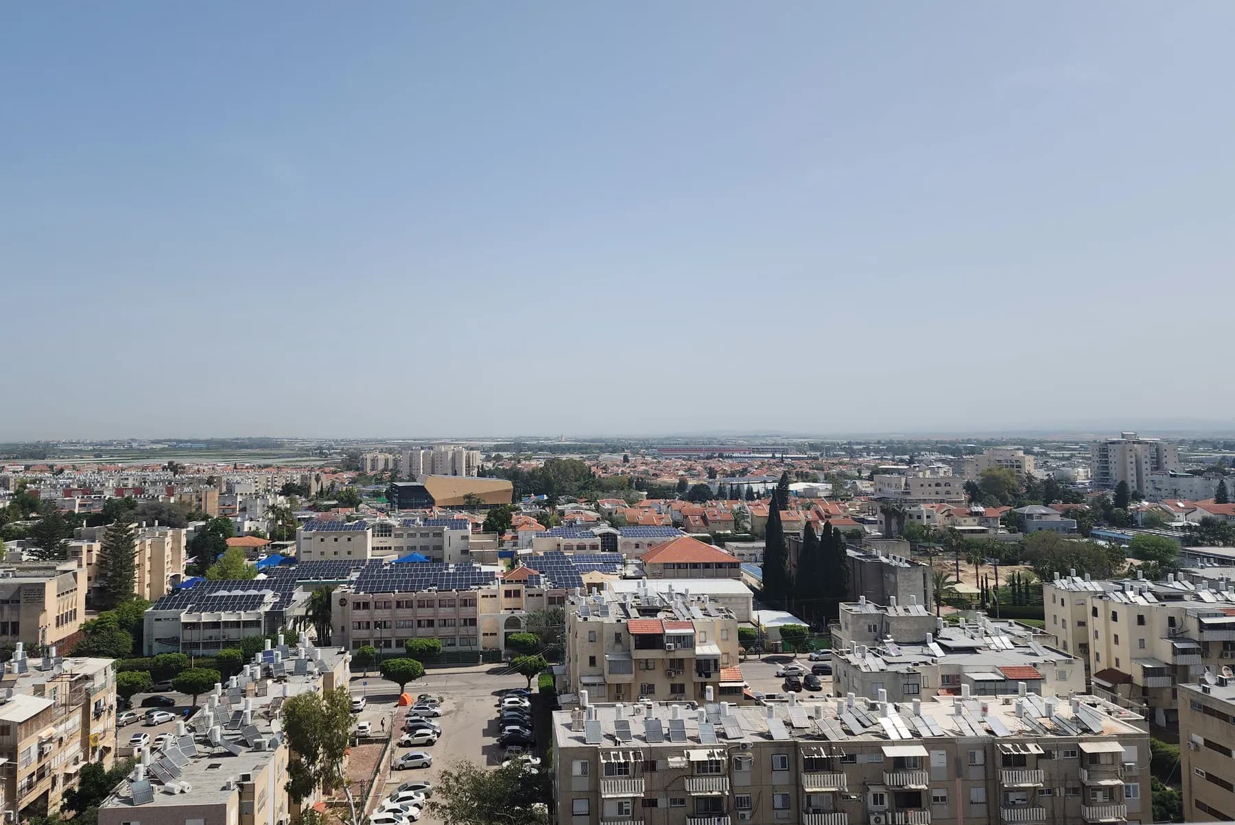 A view over the rooftops of Kiryat Malachi, with apartment blocks, solar water heaters and trees.
