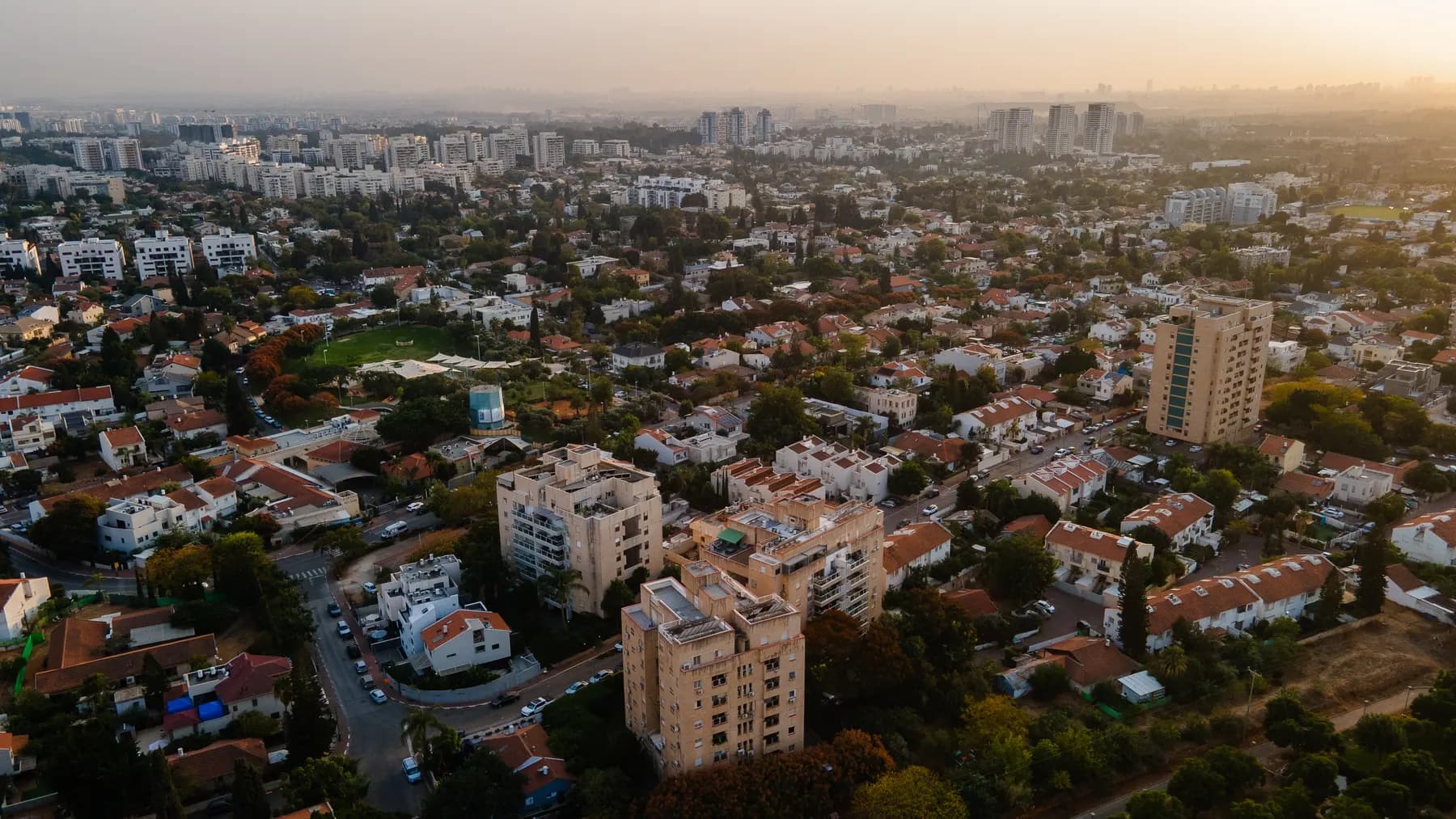 An aerial view over Kiryat Ono at sunset, with houses, apartment blocks and trees.