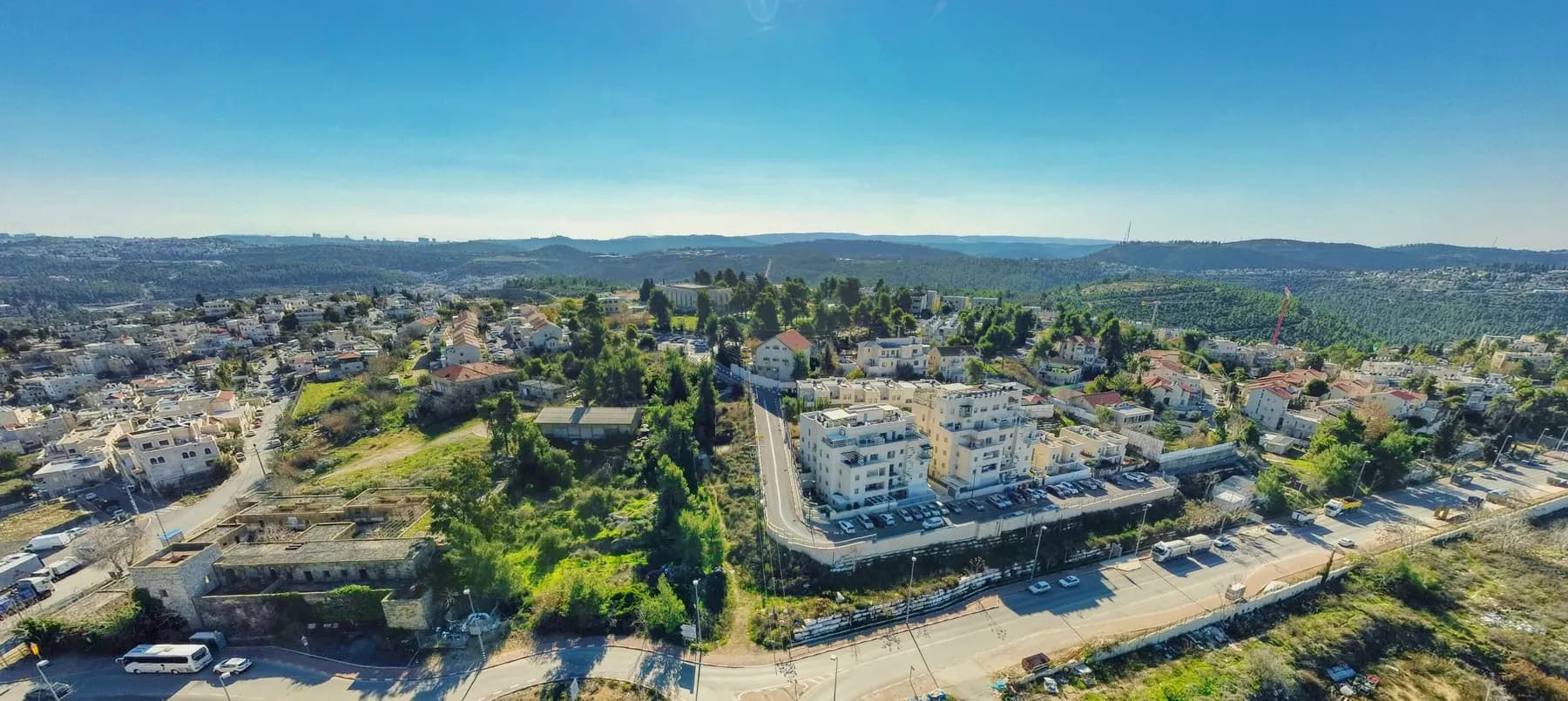 A view over Kiryat Ye'arim, with white apartment buildings and houses among trees and wooded hills stretching behind.
